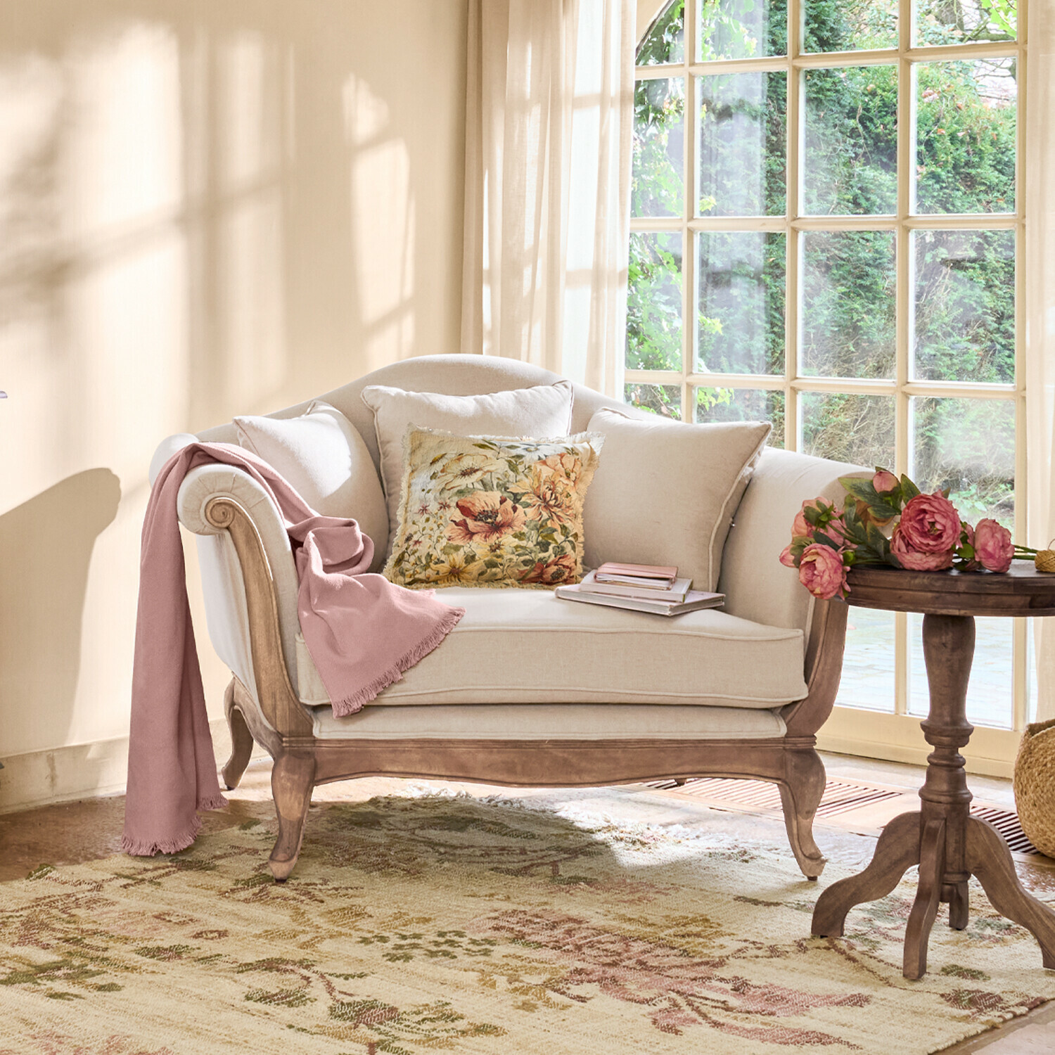 Béžová pohovka s dřevěným rámem, květinovým polštářem a růžovou dekou v světlém obývacím pokoji