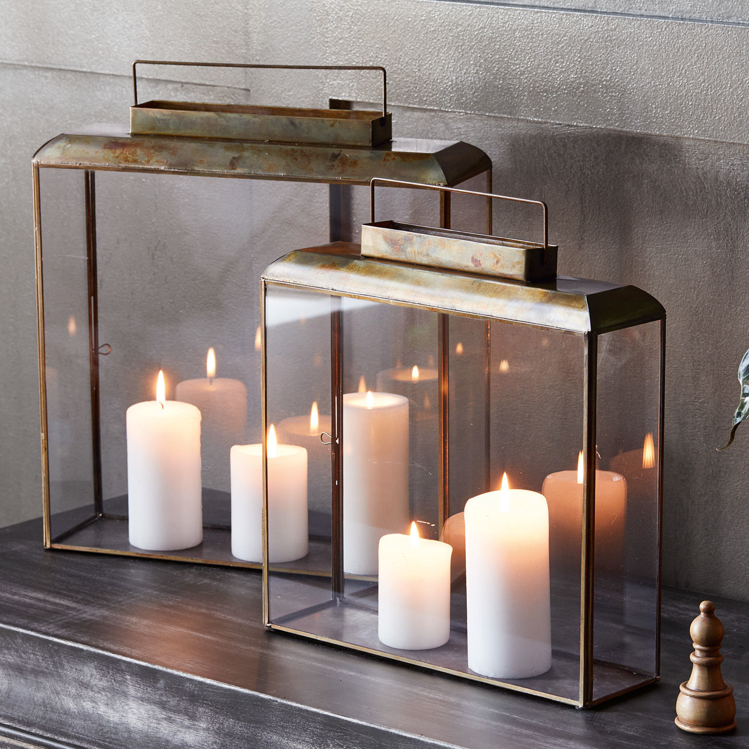 Lucerny, 2dílná sada Estrelle Dva kovové lucerny s průhledným sklem a bílými svíčkami na tmavém povrchu