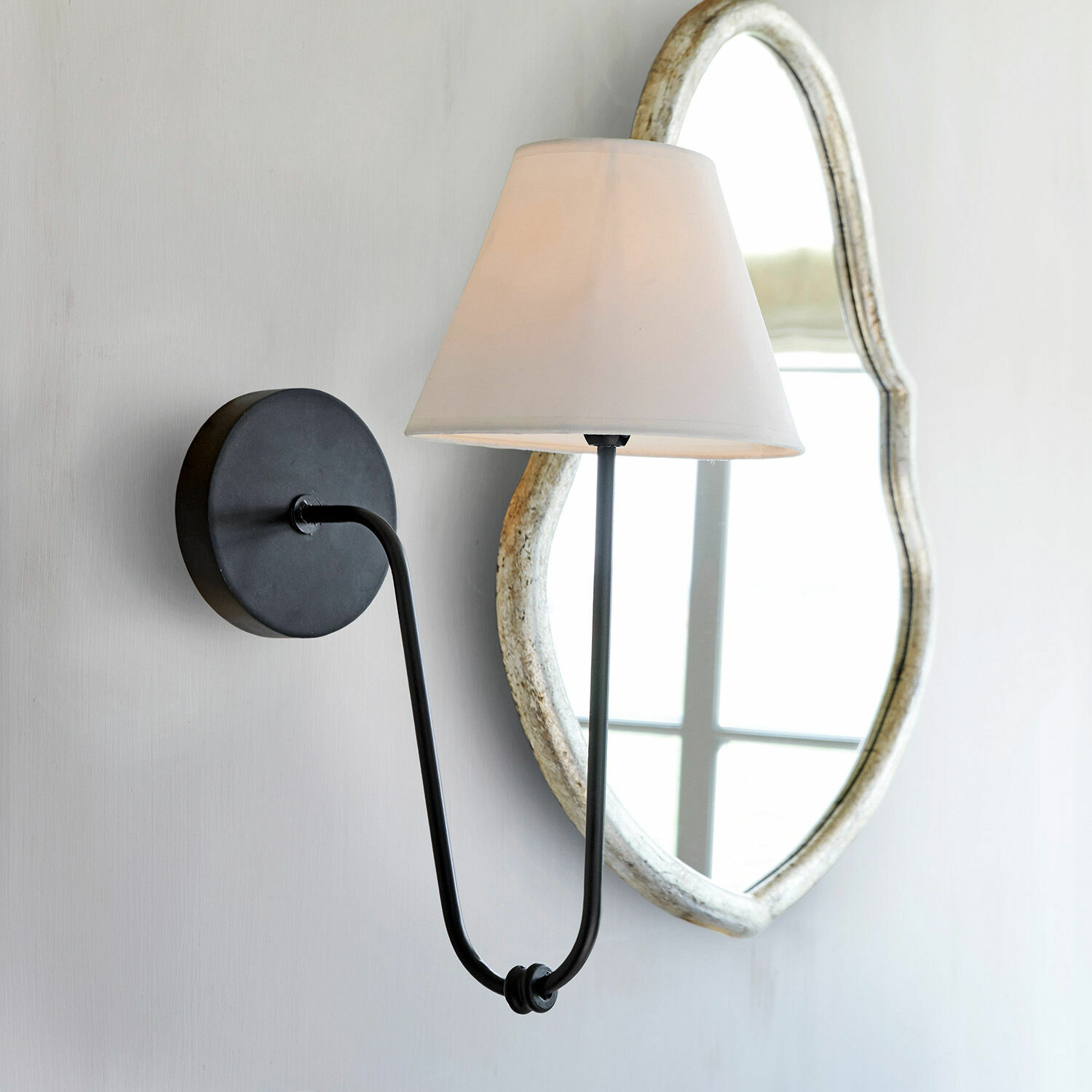 Nástěnná lampa Lustre Černé kovové nástěnné svítidlo s bílým stínidlem a dekorativním zrcadlem v pozadí, nástěnné osvětlení