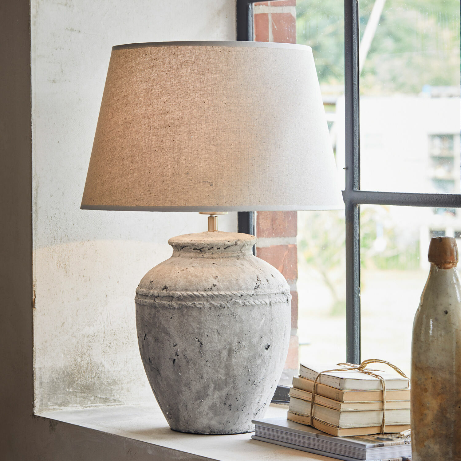 Stolní lampa Mosnay Stolní lampa ze šedé keramiky s béžovým stínidlem na parapetu vedle knih