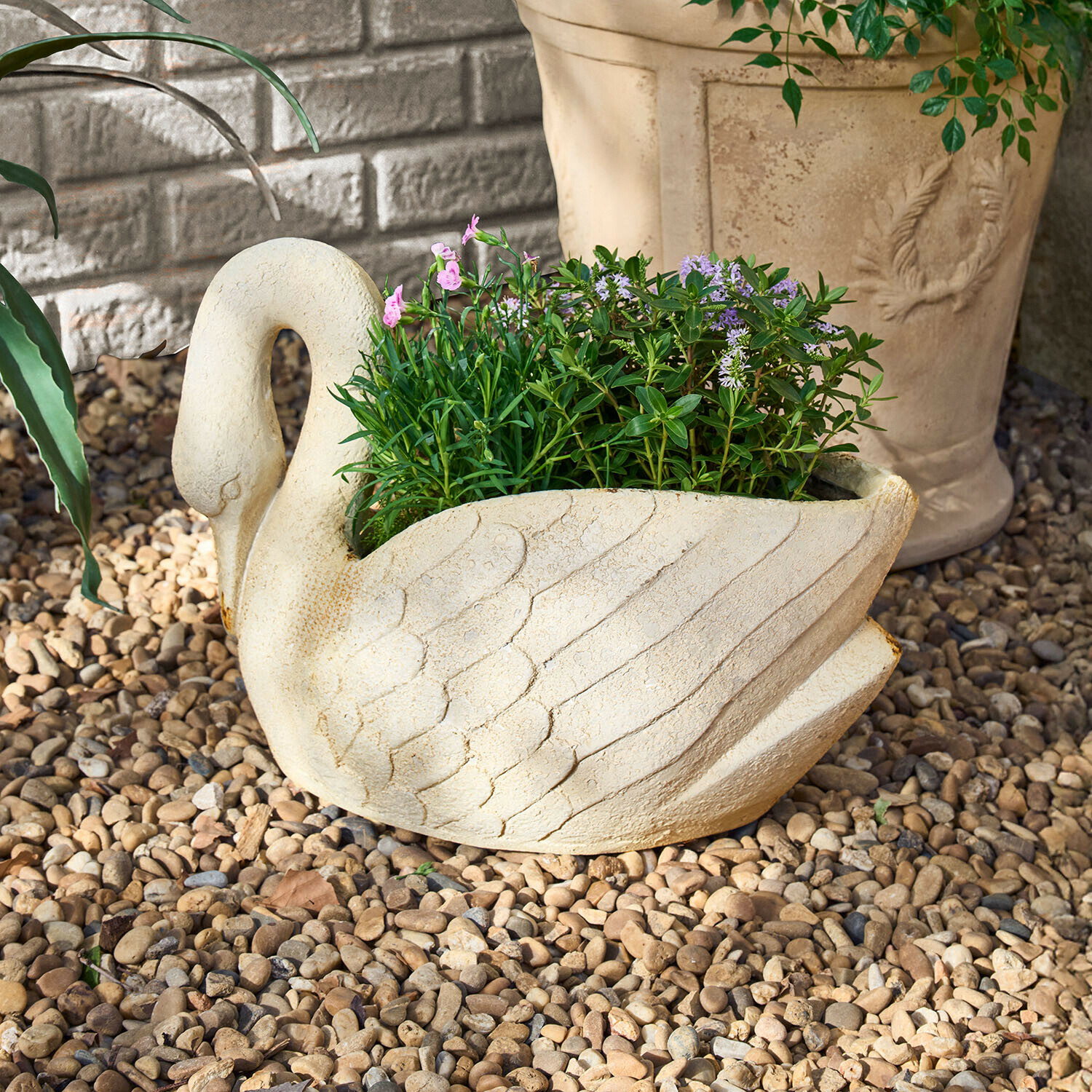 Květináč ve tvaru labutě z světlého kamene s zelenými a fialovými rostlinami na kamenné drti