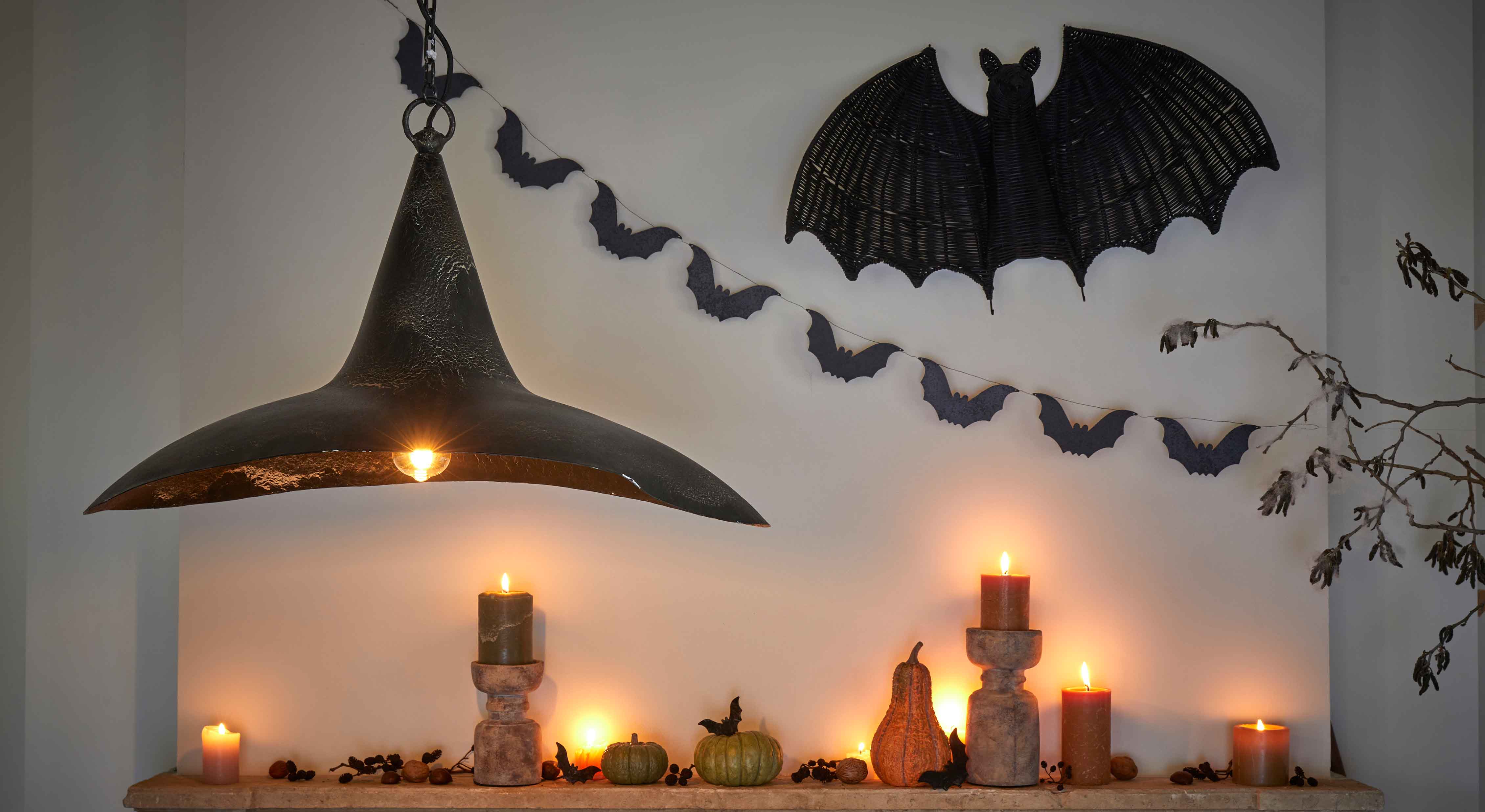 Halloween dekorace s černými svíčkami, dýněmi a černou kovovou lampou na zdi s netopýry