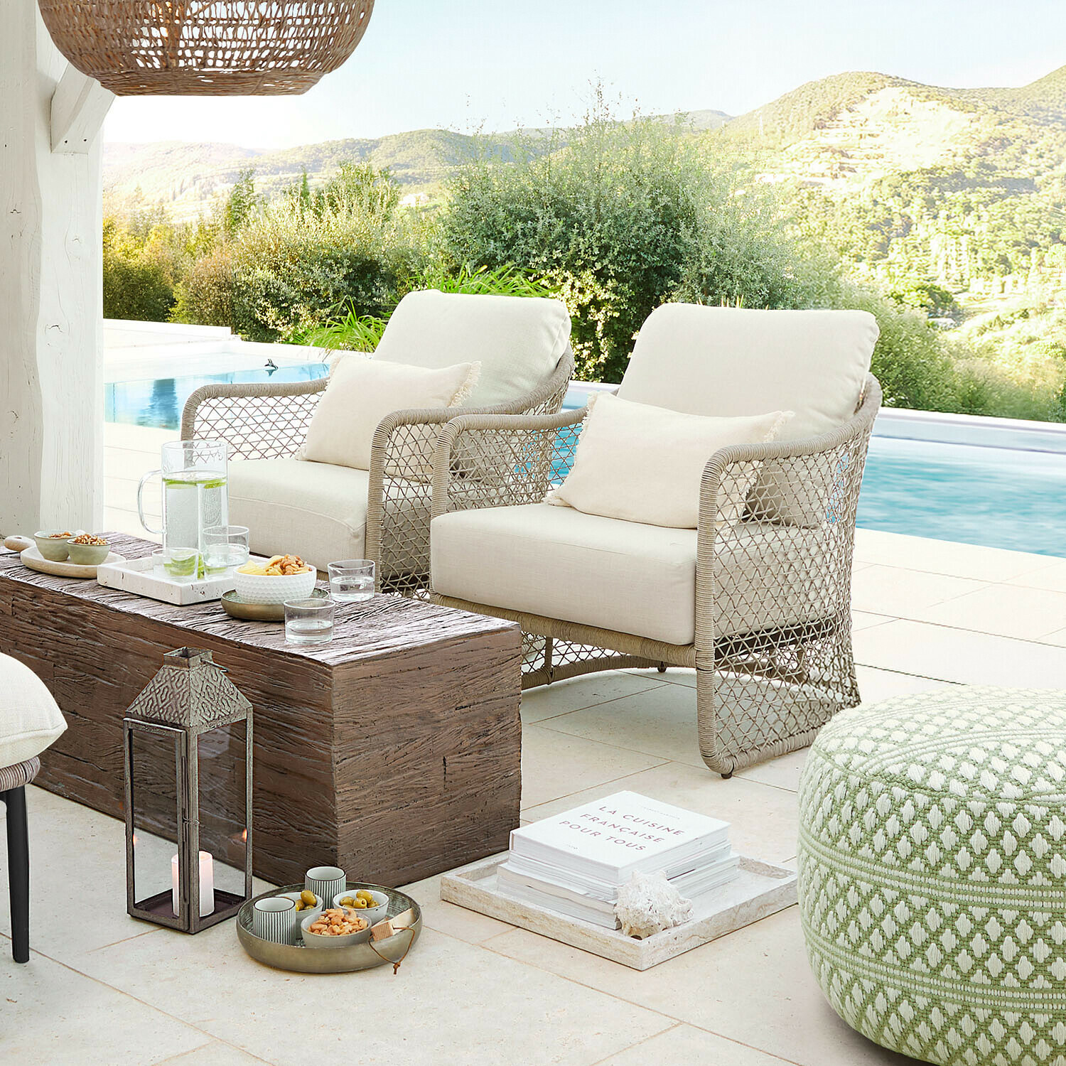 Dva béžové křesla z pleteného materiálu na terase u bazénu s dřevěným stolkem a zeleným pufem