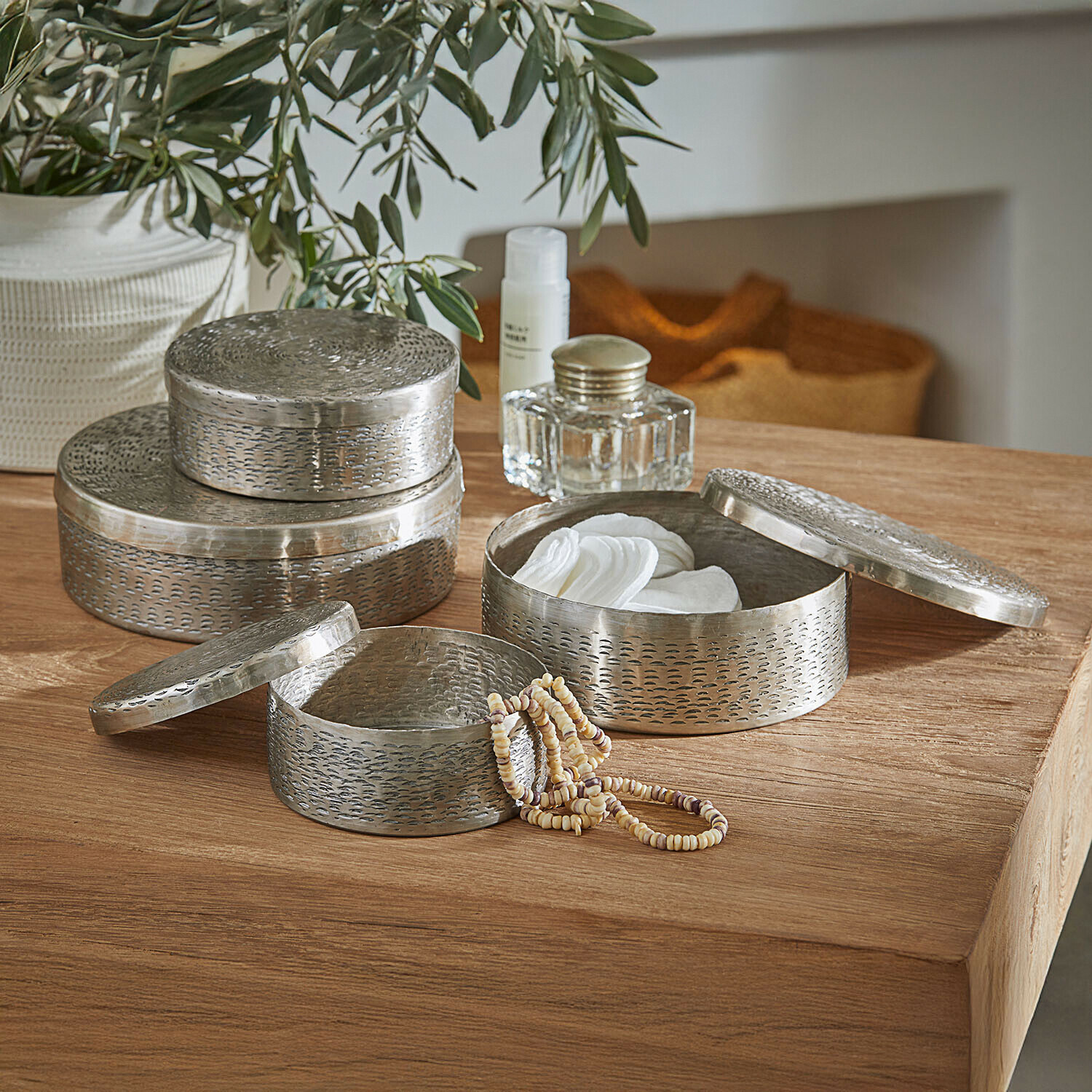 Sada tří kulatých kovových nádob ve stříbrné barvě na ukládání kosmetiky a šperků na dřevěném stole