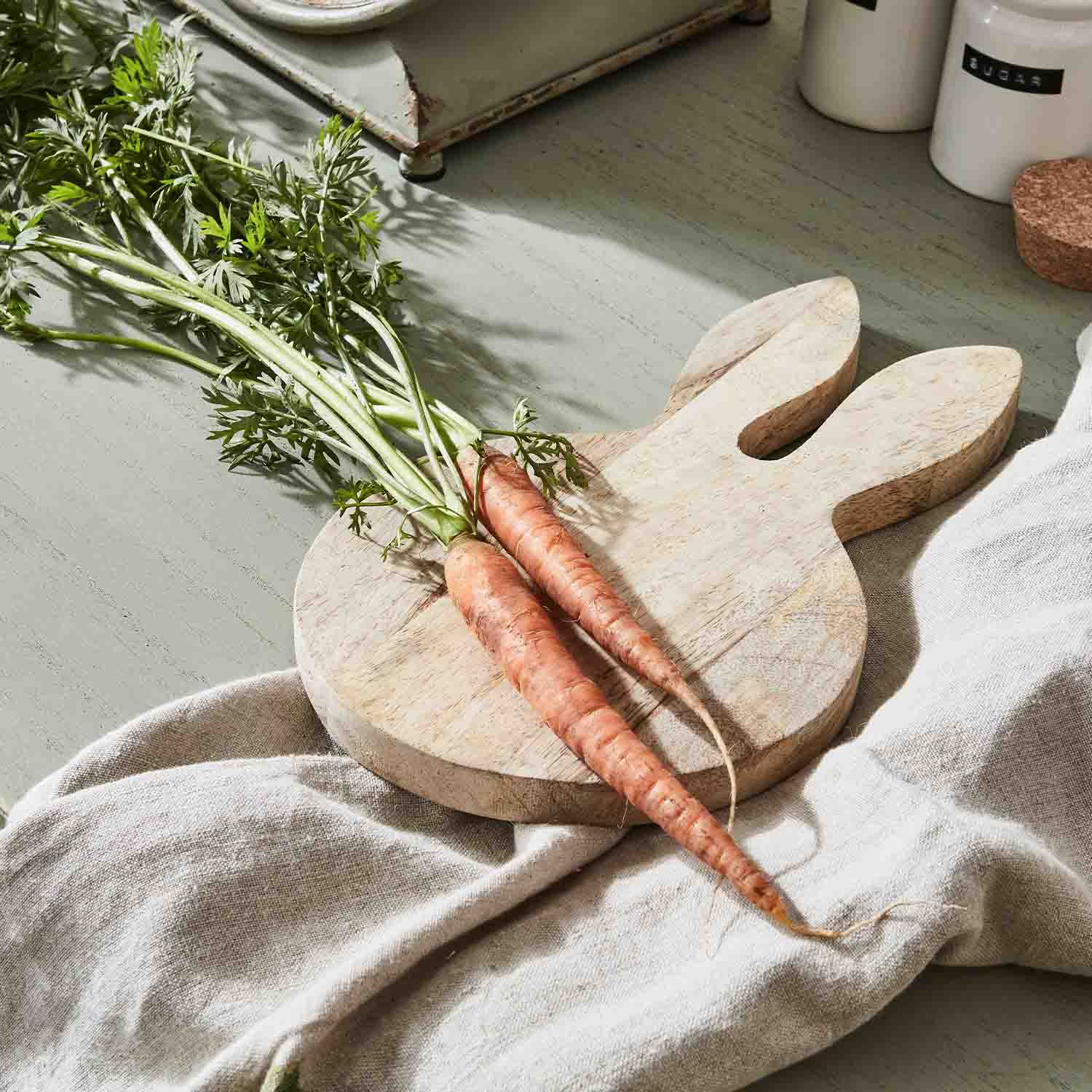 Dřevěná krájecí deska ve tvaru zajíce se dvěma čerstvými mrkvemi na lněné látce