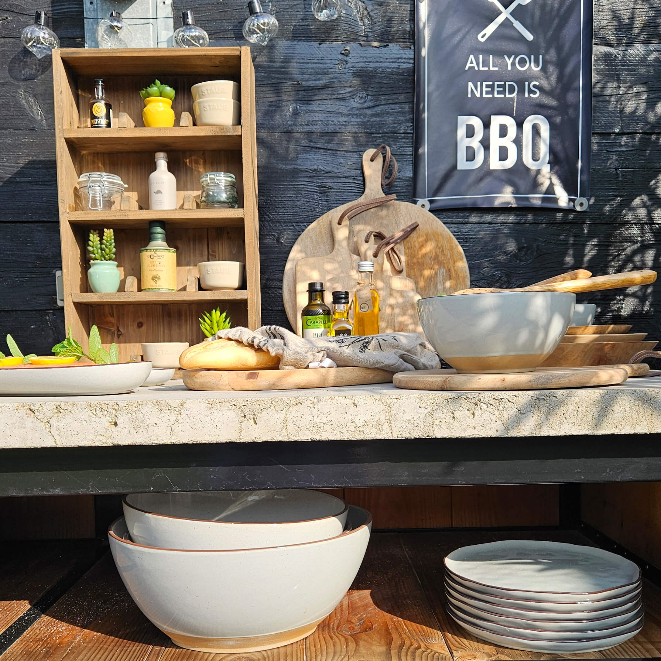 Sada béžových keramických misek a talířů s dřevěnými prkénky a lahvemi oleje na grilovacím stole