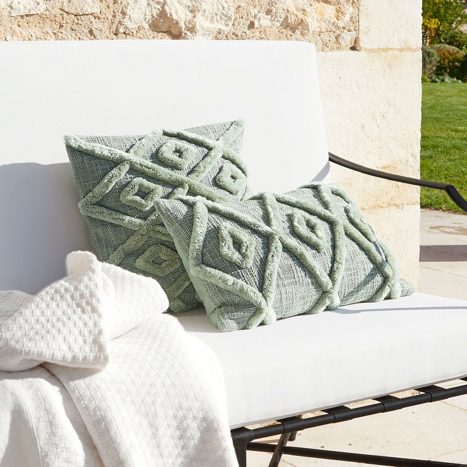 Mátově zelené dekorativní polštáře s geometrickým vzorem na bílém gauči s dekou, bytový textil