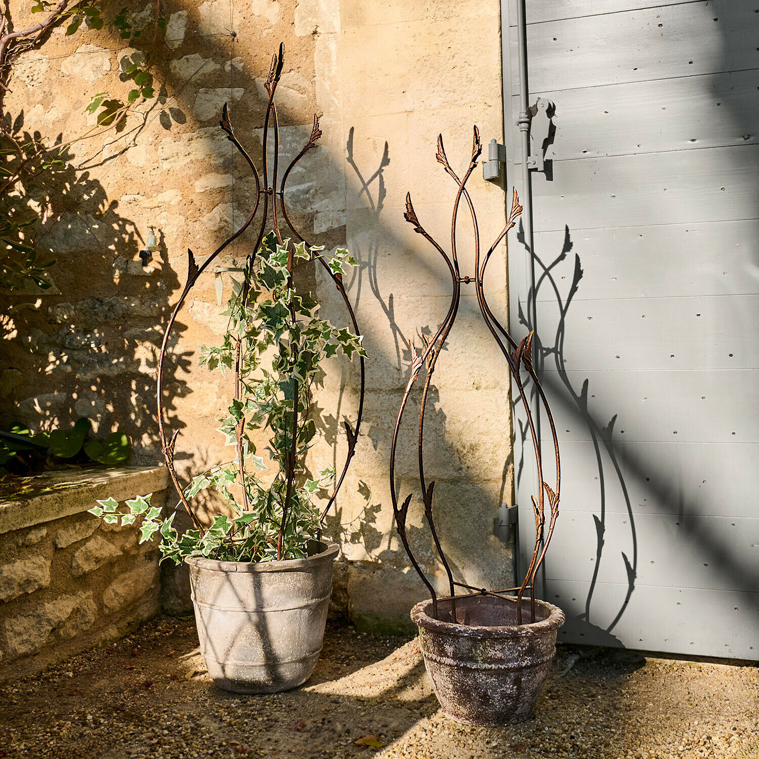 Dva ozdobné kovové opory na rostliny v kamenných květináčích na zahradní terase