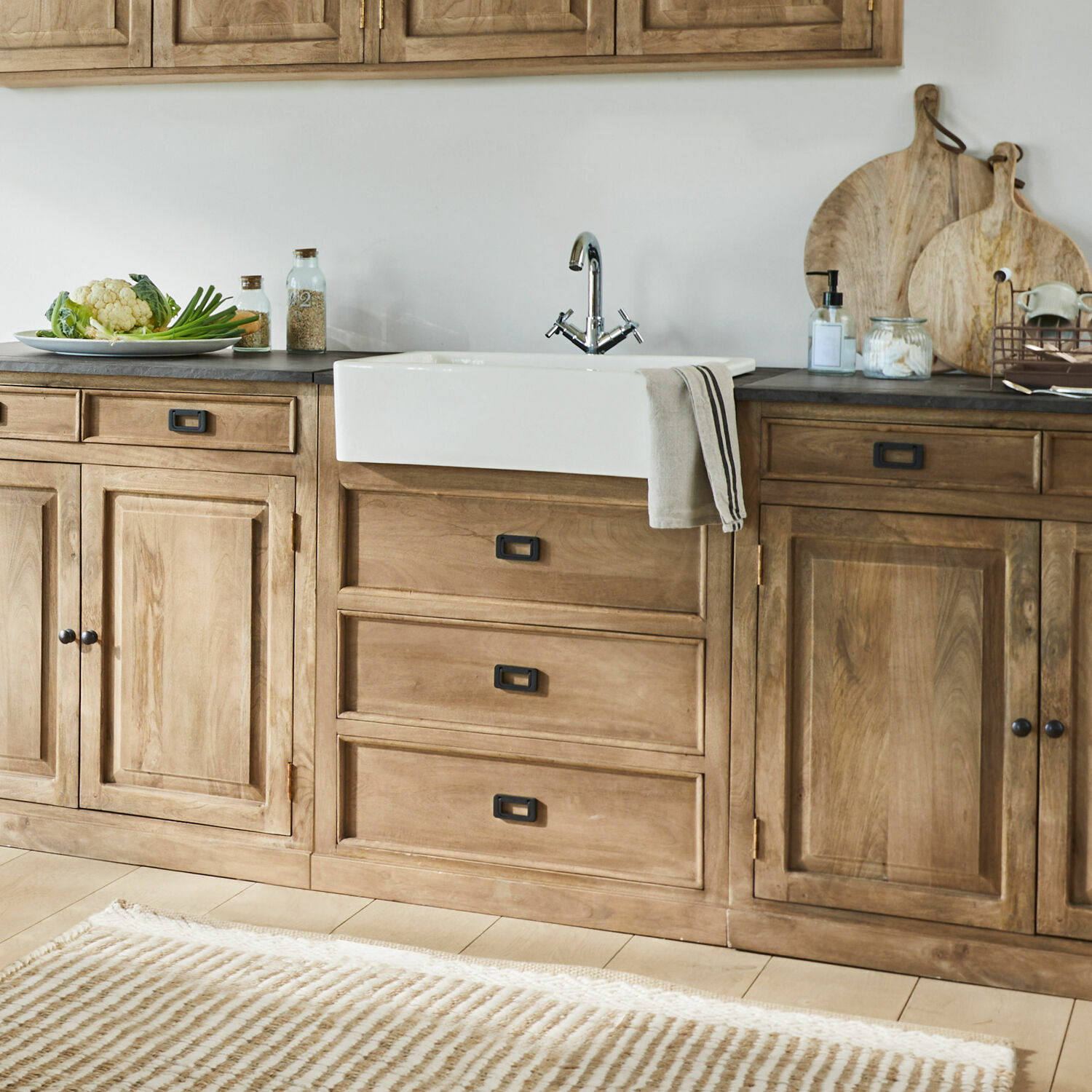 Kuchyně s dřevěnými skříňkami, bílým keramickým dřezem a pruhovaným béžovým kobercem