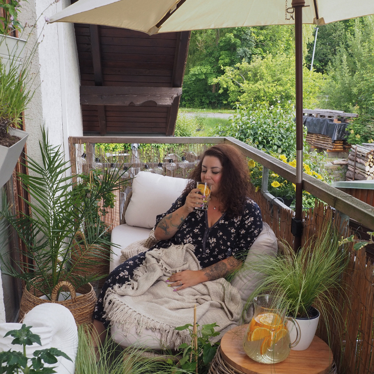 Žena odpočívá na balkoně s rostlinami, pije nápoj, relaxace v zeleném prostředí