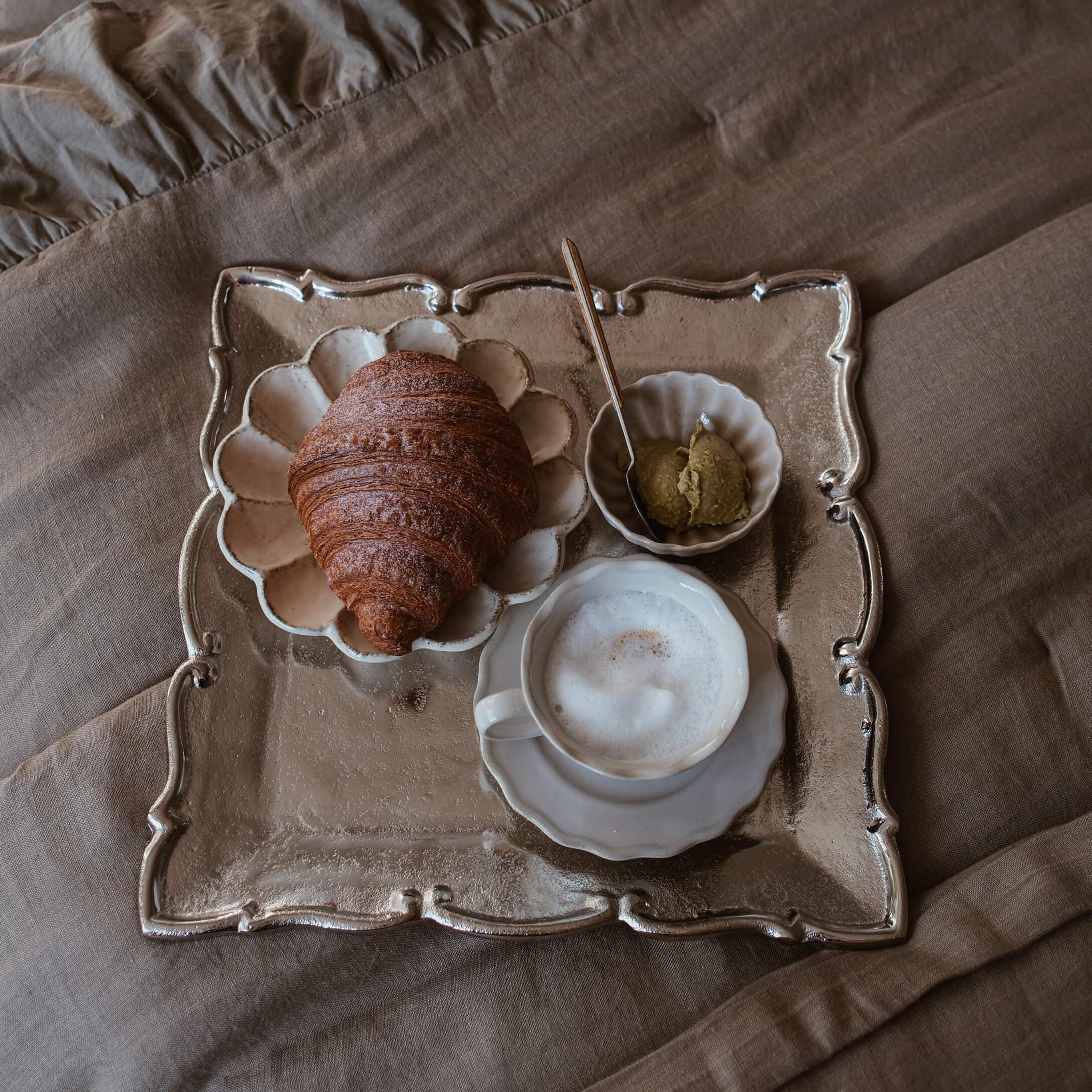 Podnos s croissantem, kávou s pěnou a pomazánkou na béžové látce ve stylu slow living