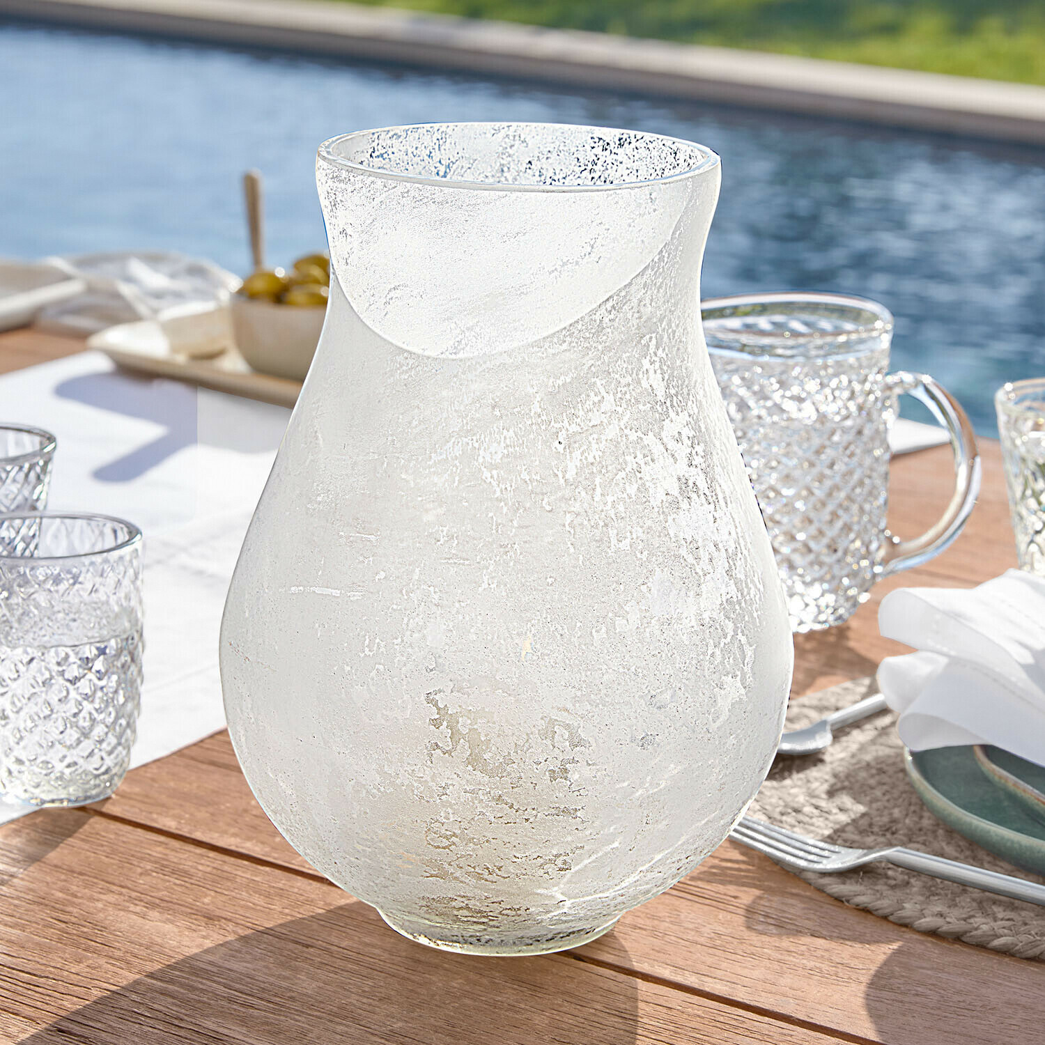 Průhledná karafa z matného skla na dřevěném stole, vhodná pro podávání nápojů venku