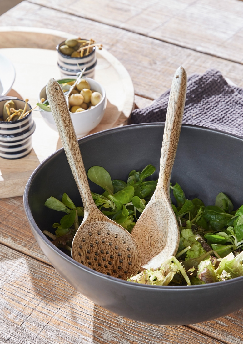 Černá mísa s dřevěnými lžícemi na salát a zeleným salátem na dřevěném stole