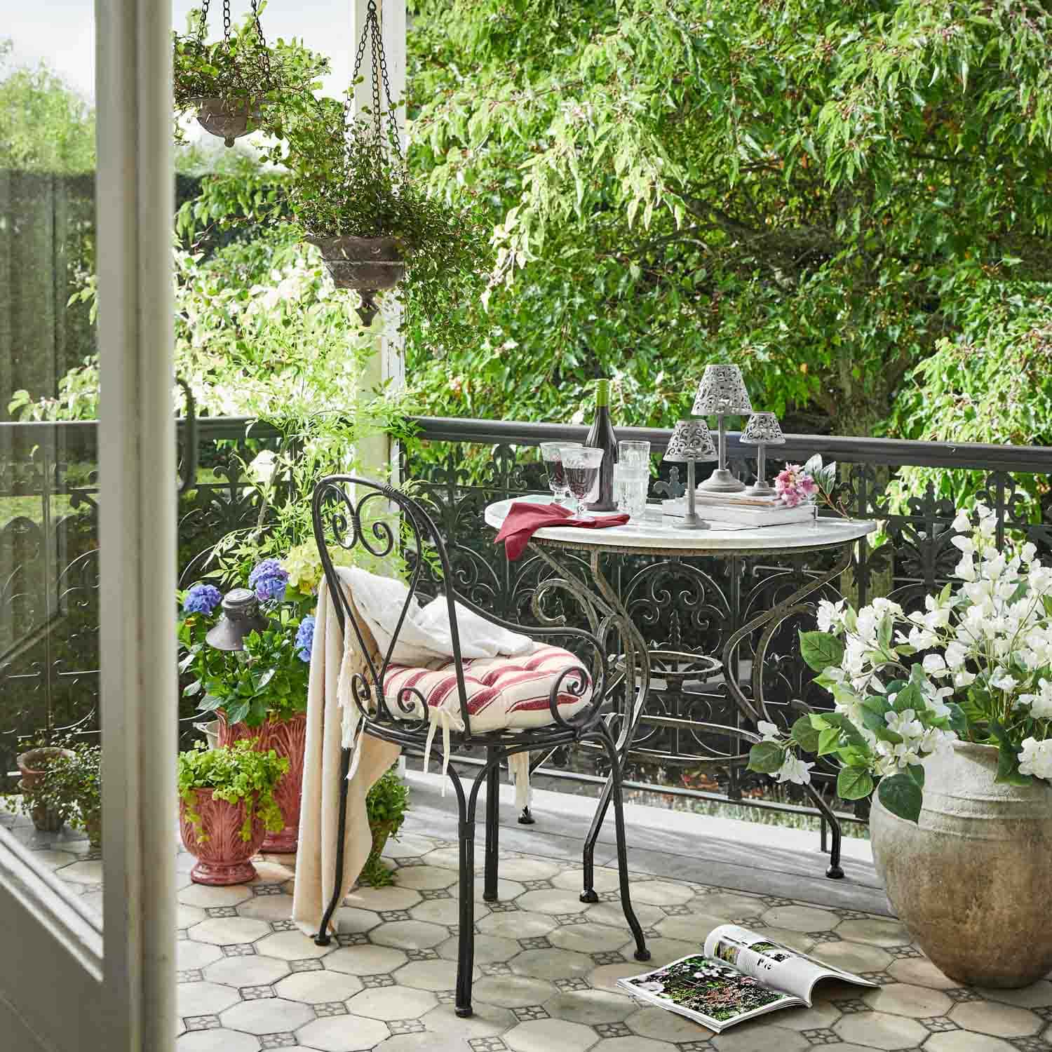 Balkon s kovovým stolem a židlí, květiny v květináčích, relaxační venkovní prostředí