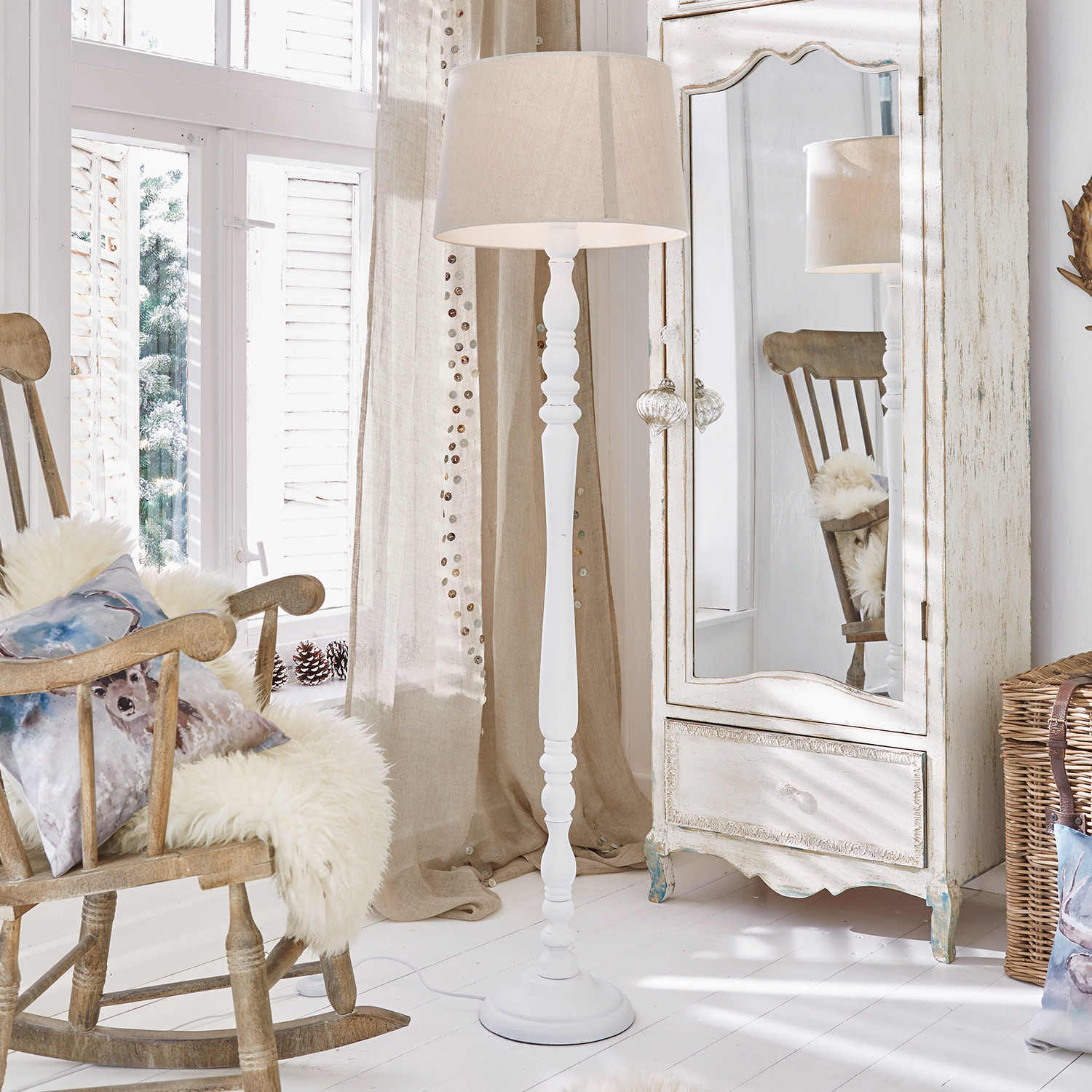 Stojací lampa Statford Bílá dřevěná stojací lampa s béžovým stínidlem v světlém rustikálním interiéru se zrcadlem a houpacím křeslem