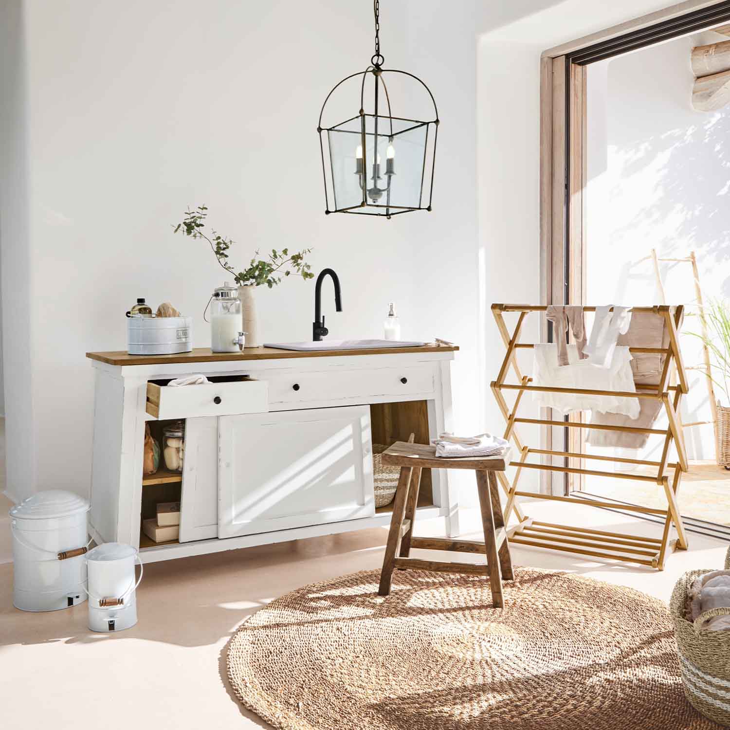 Bílá dřevěná komoda s přírodním dřevěným povrchem a černou baterií v světlé místnosti se sušákem na prádlo