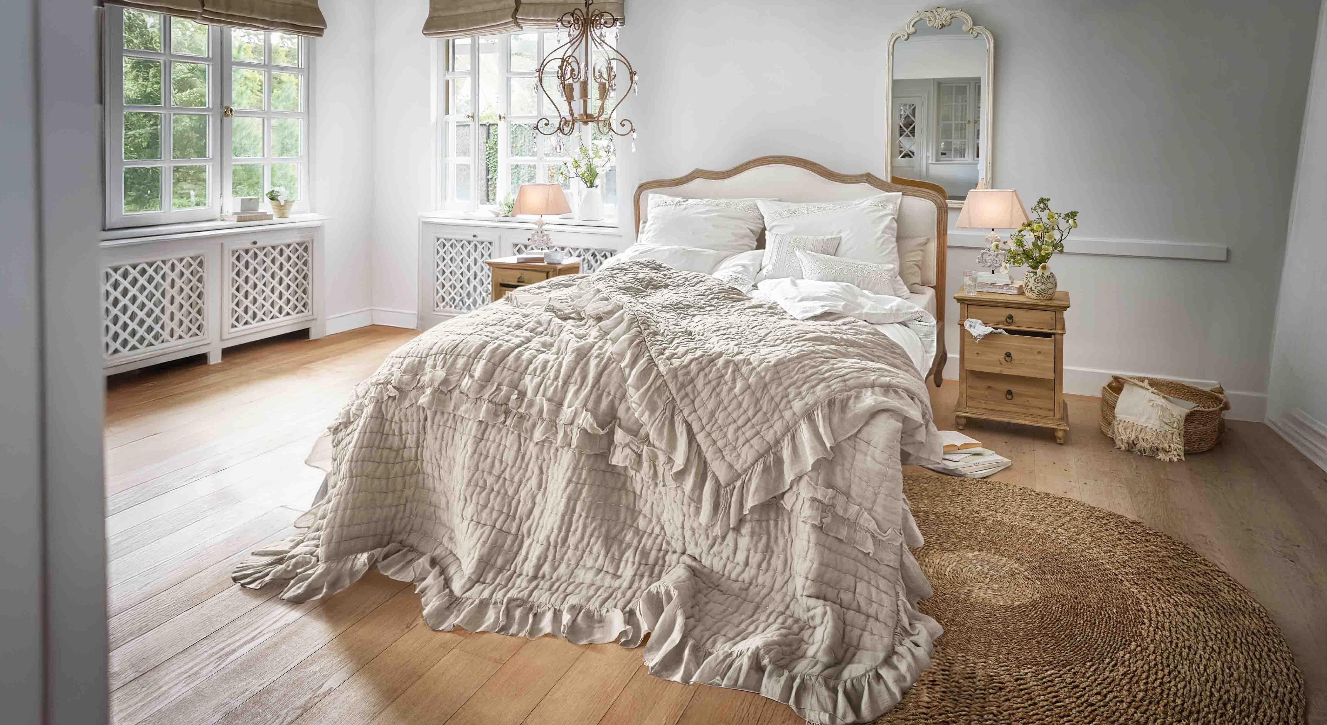 Pohodlná ložnice s postelí v béžovém přehozu s volánky a dřevěným nábytkem