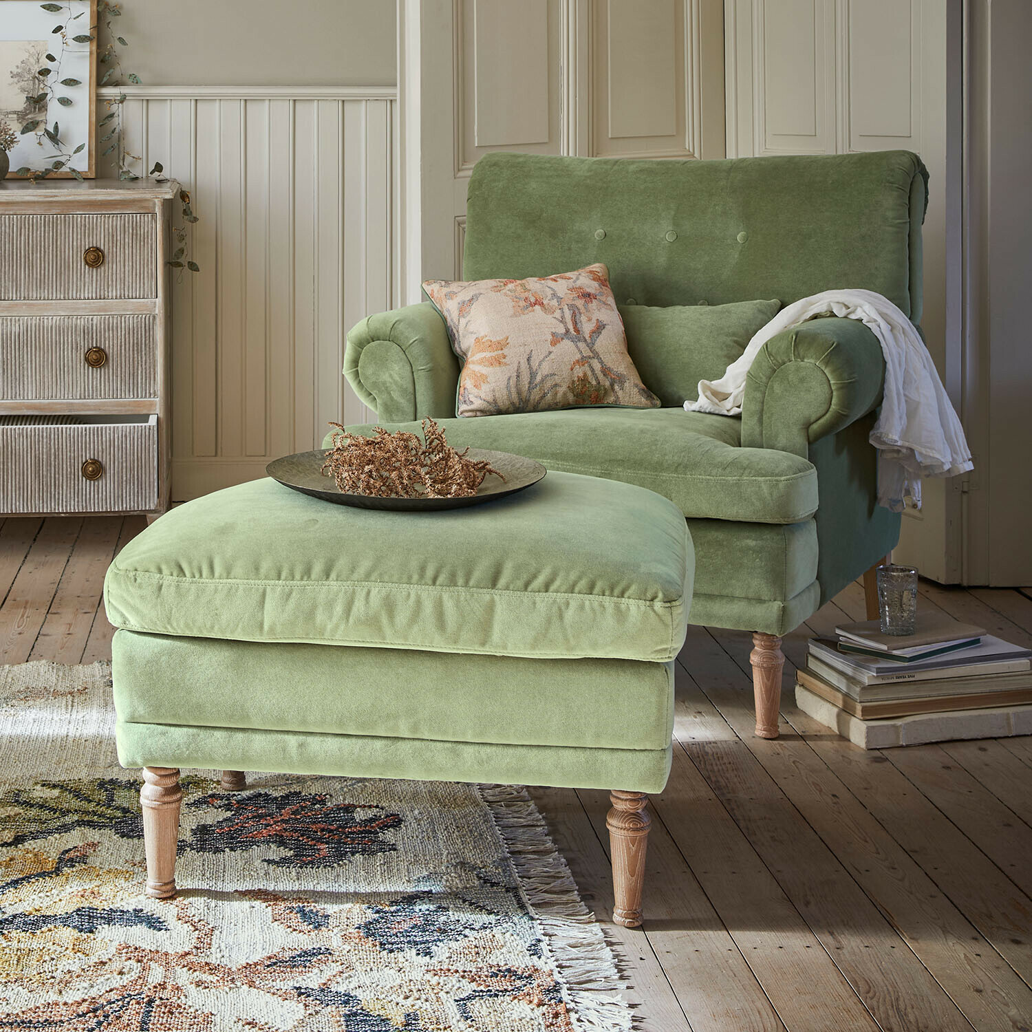 Zelené sametové křeslo s podnožkou na dřevěných nohách v útulném obývacím pokoji s kobercem