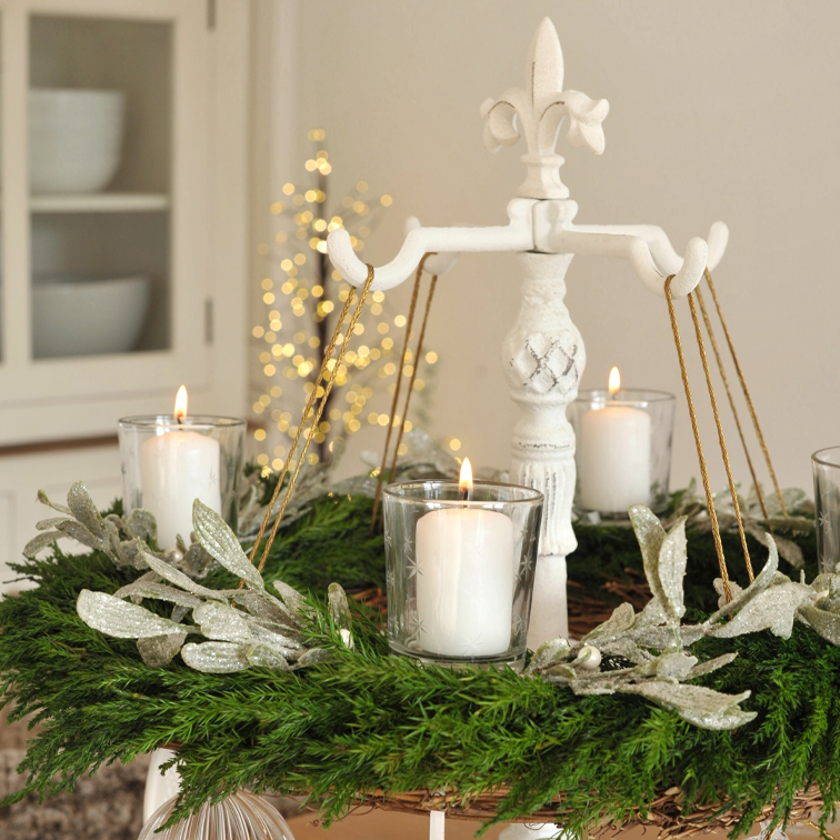 Bílý kovový adventní věnec se zelenými větvemi a bílými svíčkami, vánoční dekorace