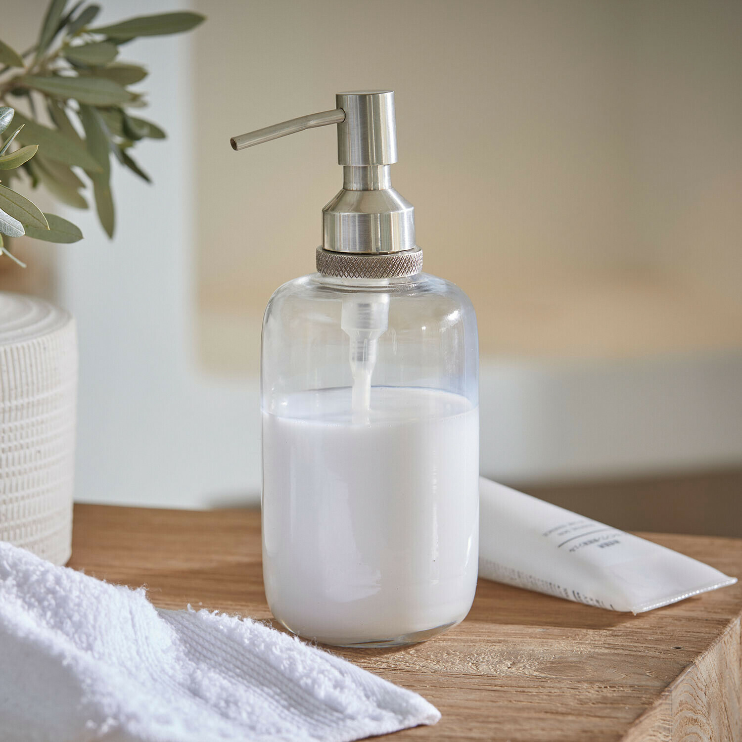 Průhledný dávkovač mýdla z nerezové oceli s bílou tekutinou na dřevěném povrchu