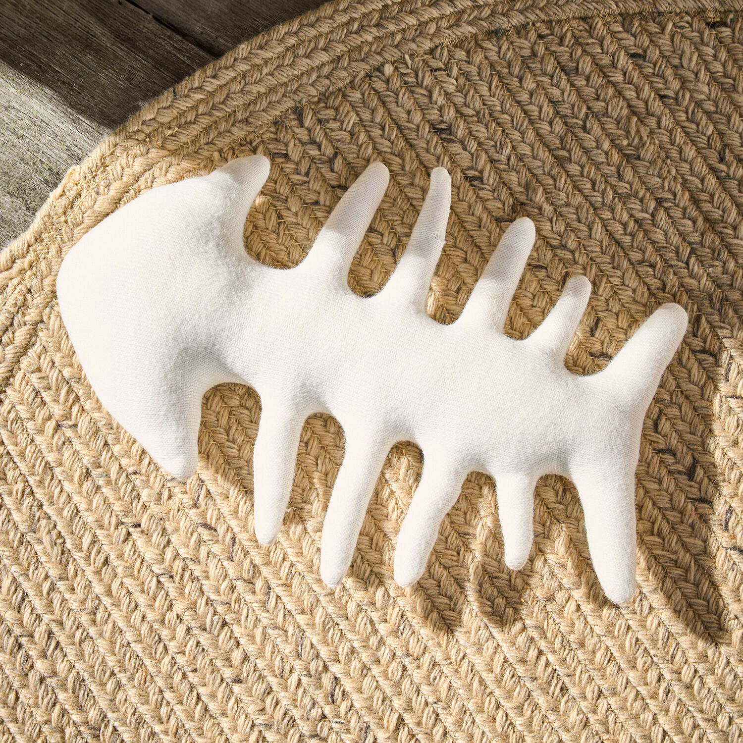 Bílá dekorace ve tvaru rybí kostry z látky na pleteném jutovém koberci