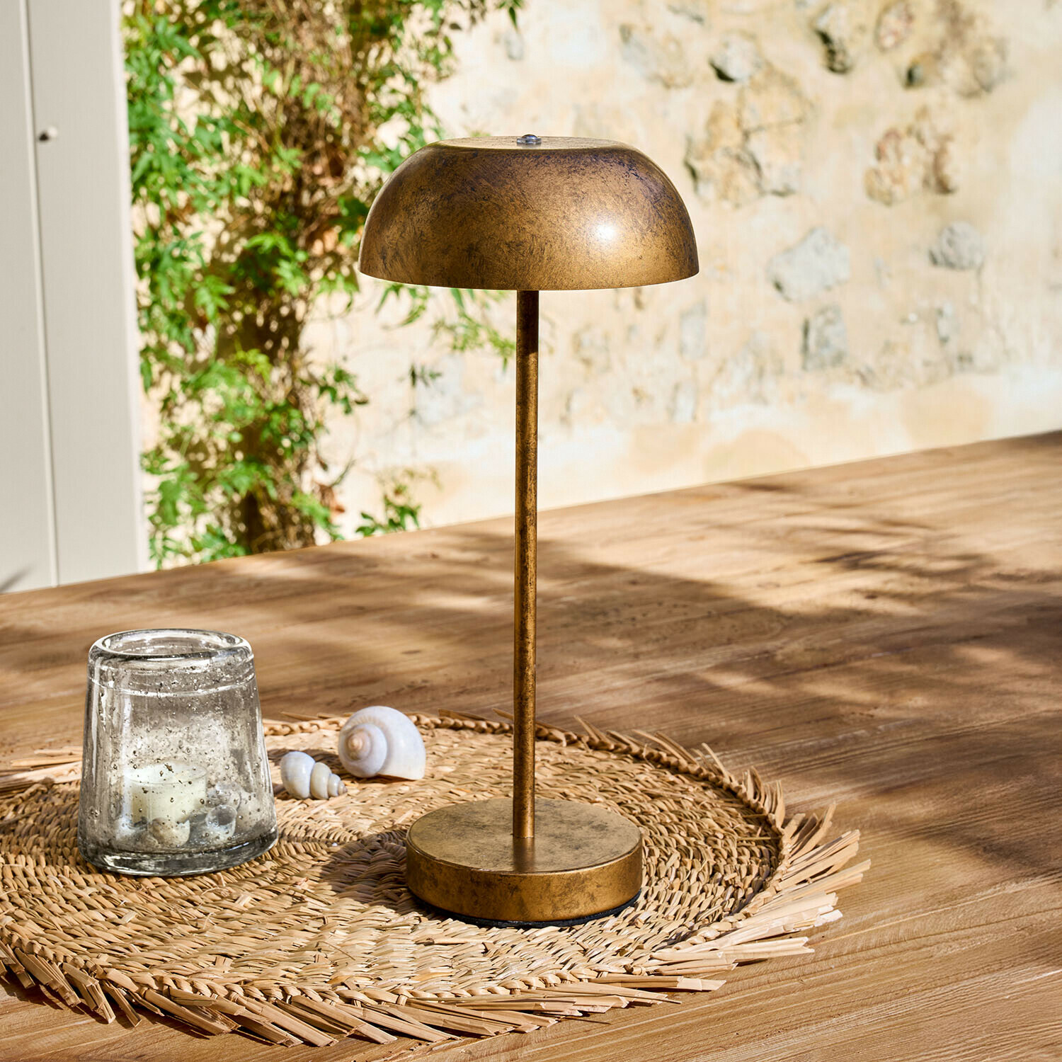 Stolní lampa z kovu ve starozlaté barvě na pleteném podložce na dřevěném stole