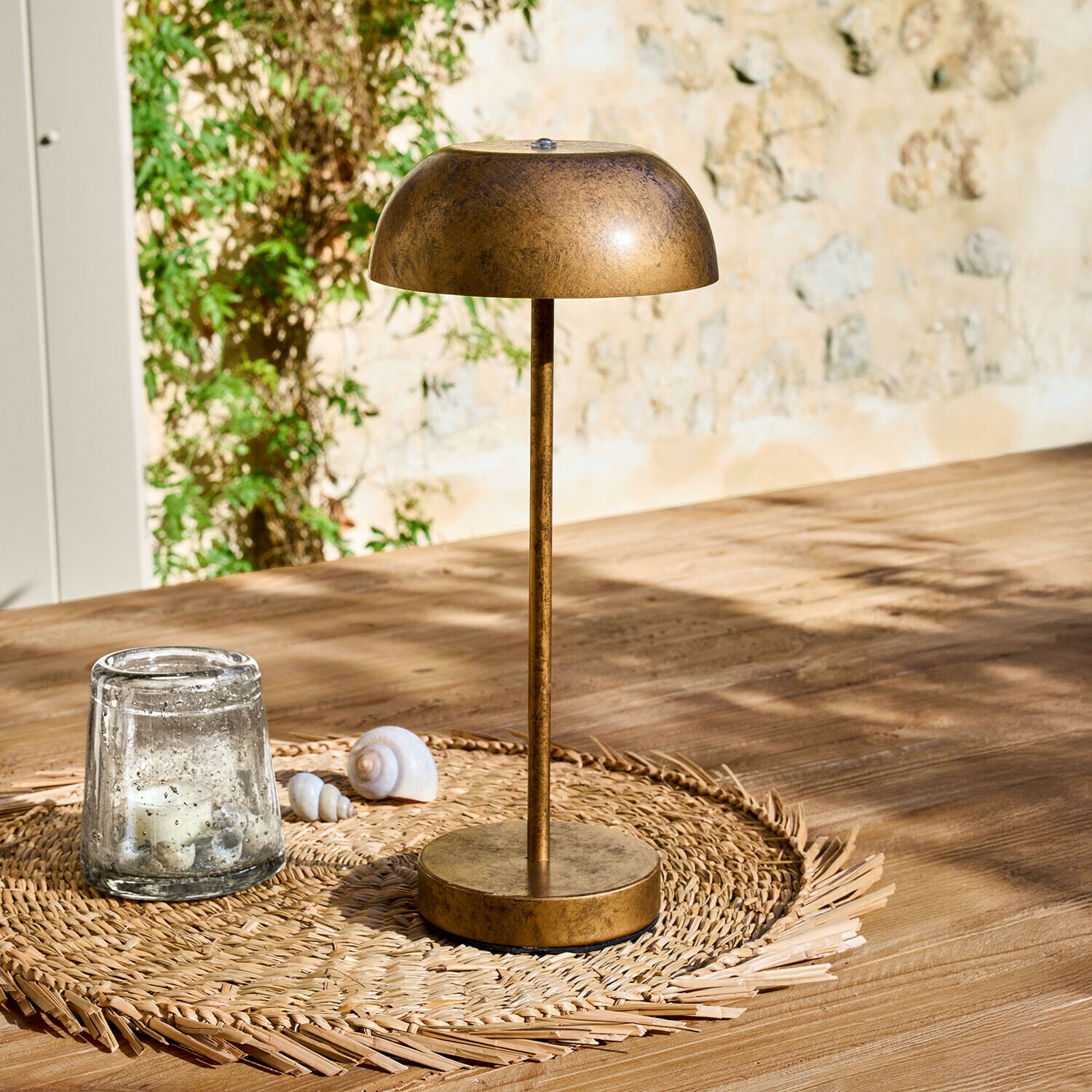 Dobíjecí stolní lampa Lumirah Stolní lampa z kovu ve starozlaté barvě na pleteném podložce na dřevěném stole