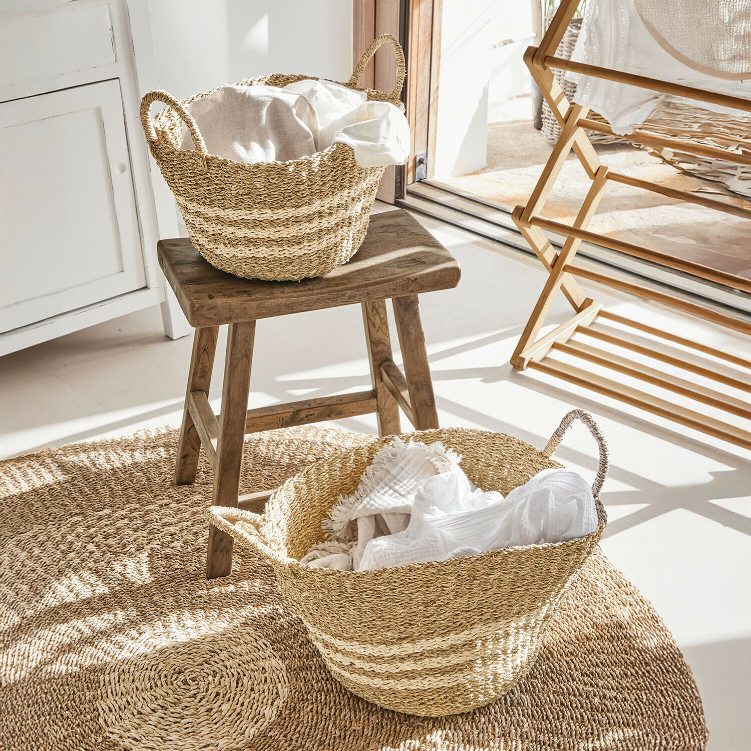 Koše z mořské trávy v přírodní barvě s bílými látkami na kulatém koberci v světlé místnosti