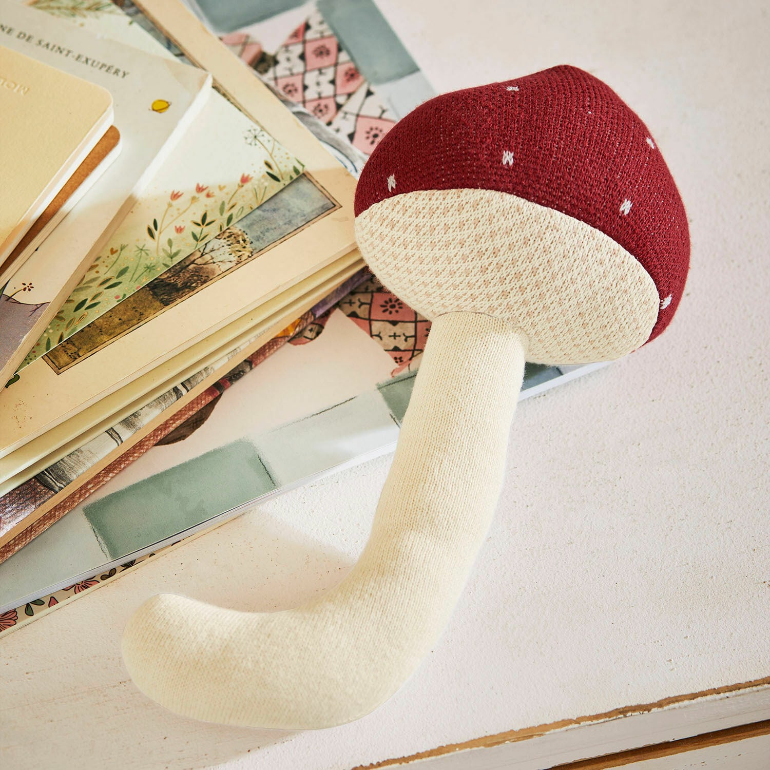 Látková hračka Norilie Měkká plyšová hračka houba v červeno-krémových barvách na stole s knihami