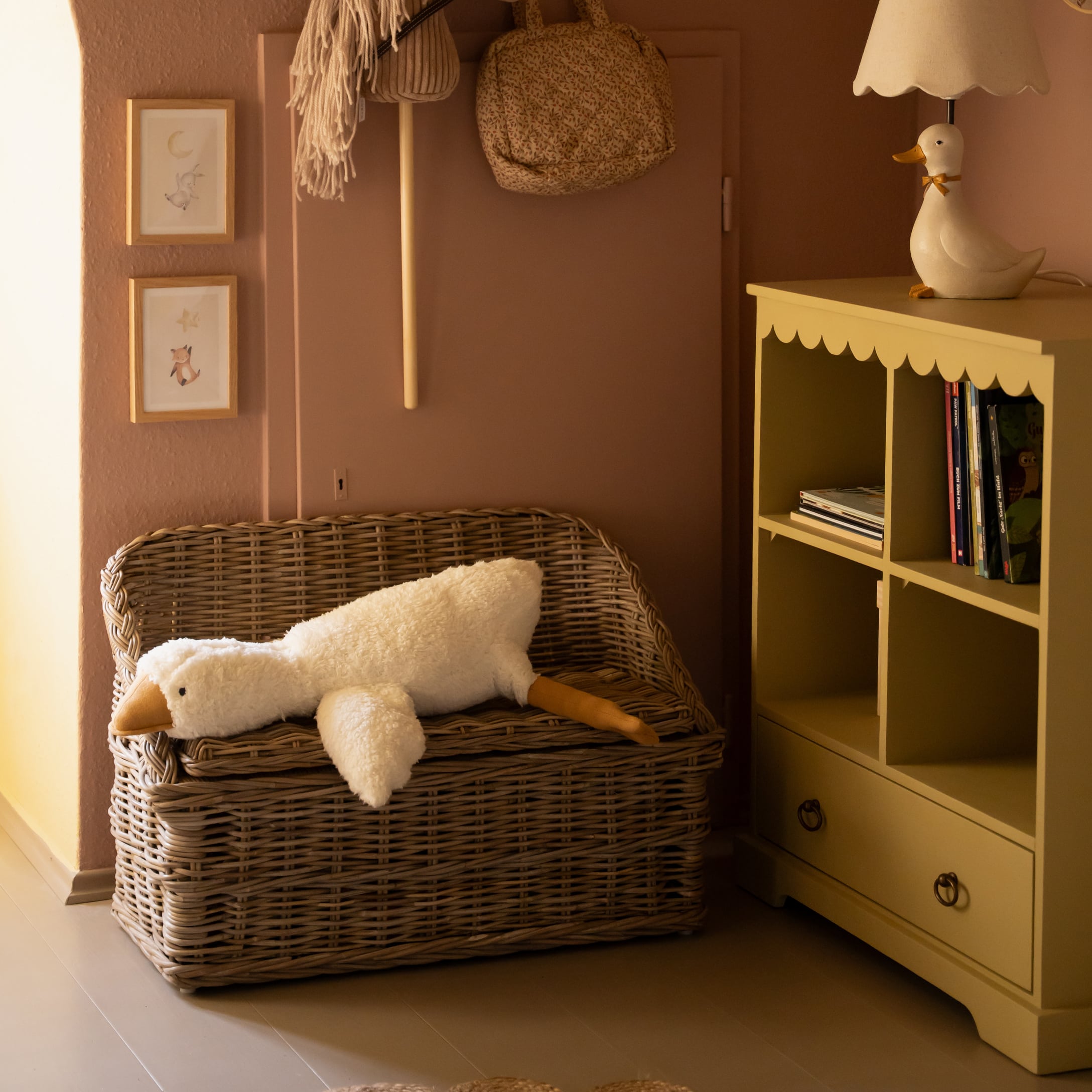 Proutěná lavice s bílým plyšovým kachním polštářem v útulném dětském pokoji se žlutou skříňkou