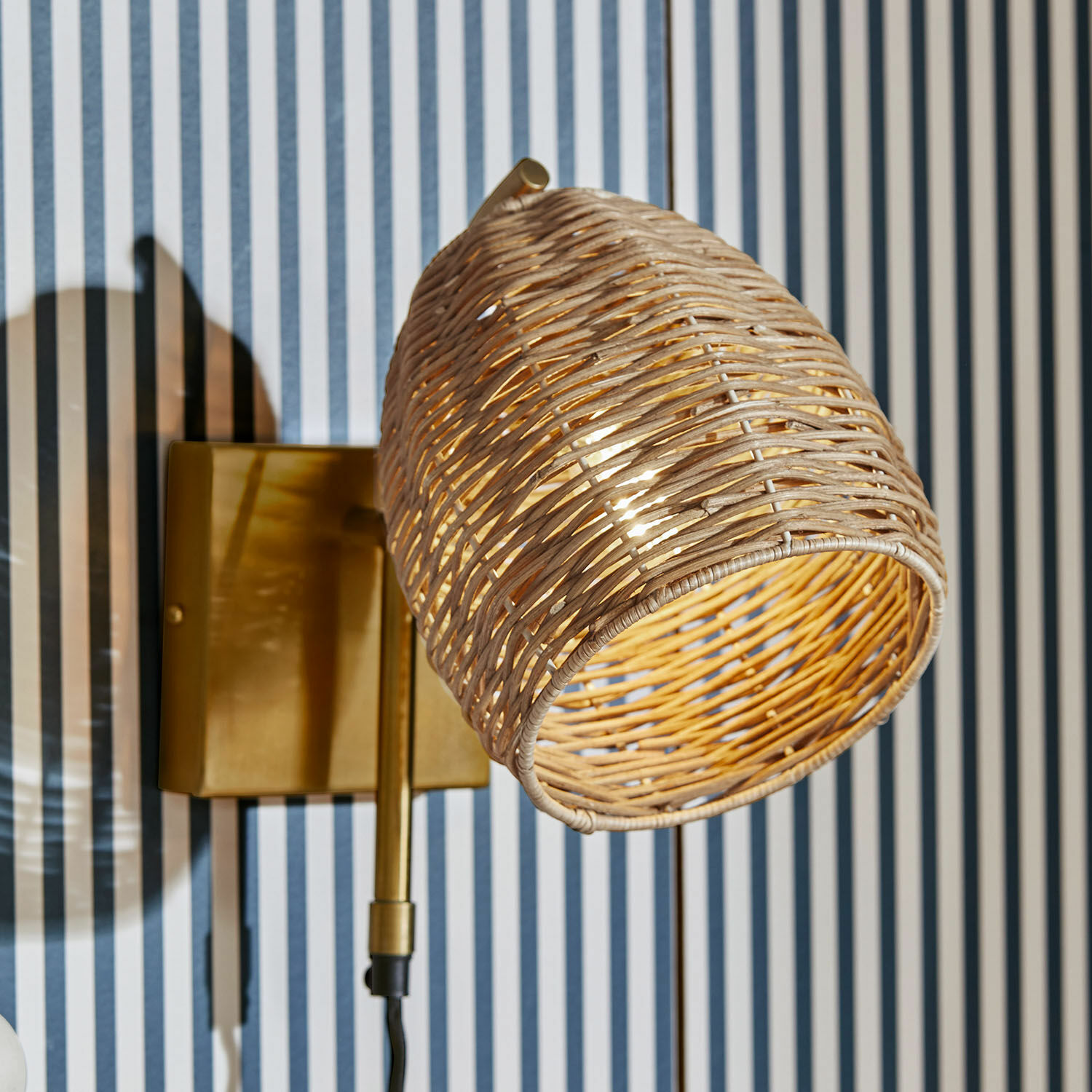 Nástěnná lampa Anglemont Nástěnné svítidlo s ratanovým stínidlem a mosazným držákem na pruhované stěně