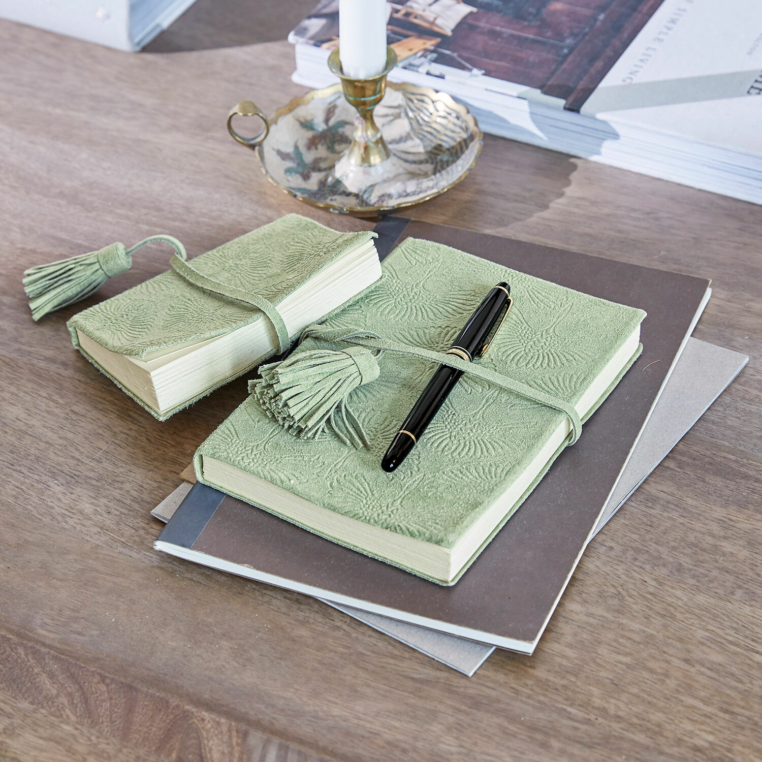 Zelený kožený zápisník s raženým vzorem a střapcem na dřevěném stole s černým perem