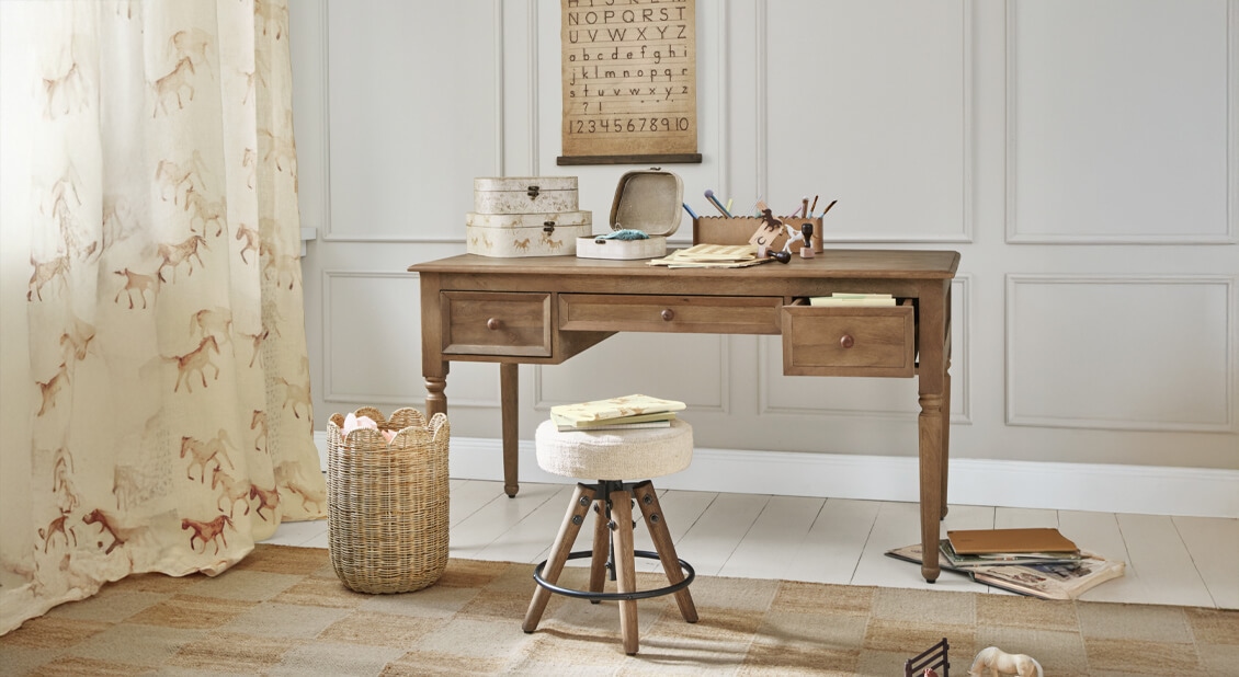 Dřevěný psací stůl se třemi zásuvkami a světlá čalouněná stolička v útulné pracovně