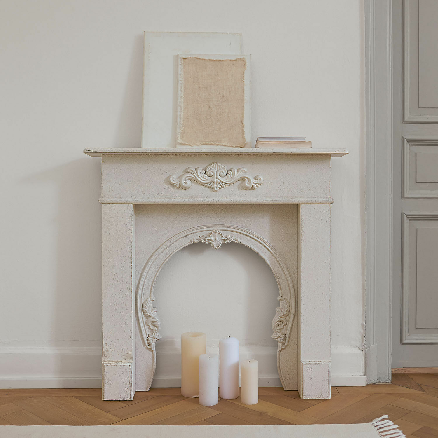 Krbová římsa Jarnéville Bílý dekorativní krbový rám s ornamenty a svíčkami na dřevěné podlaze ve vintage stylu