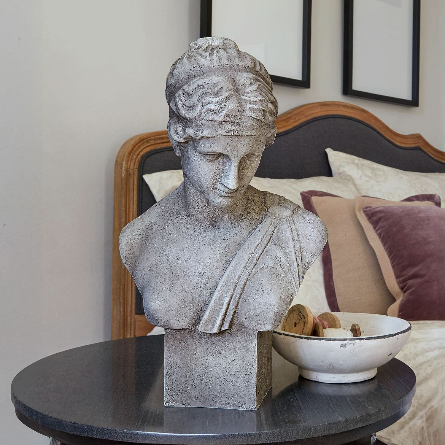 Bysta Castolio Šedý kamenný bust na černém stole v elegantním interiéru s polštáři
