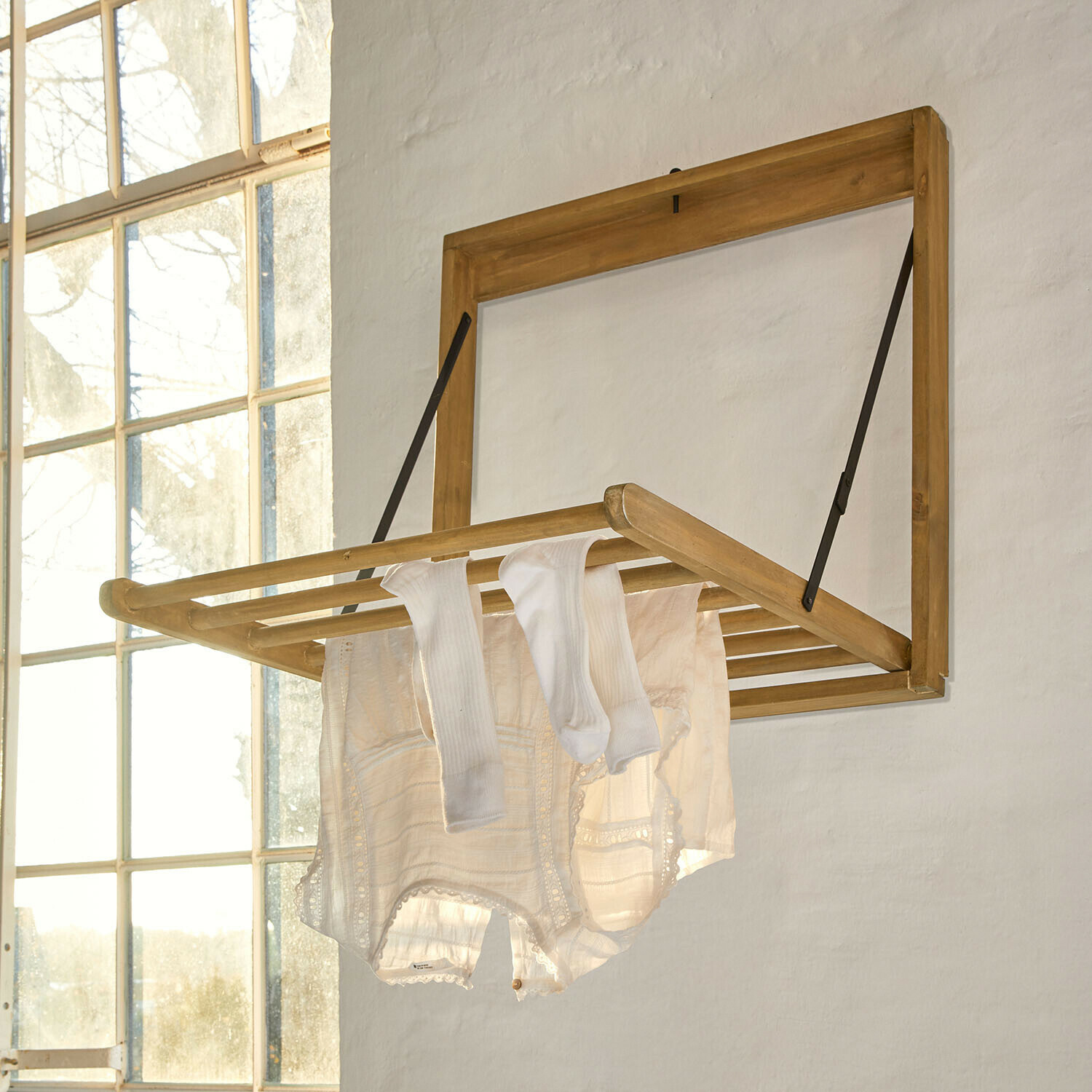 Skládací nástěnný sušák z jasného dřeva s bílým prádlem v světlé místnosti