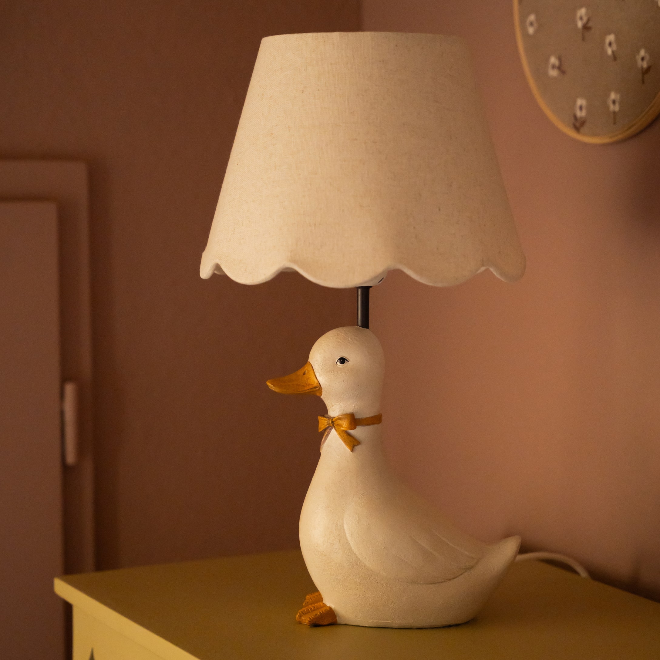 Stolní lampa ve tvaru bílé kachny s béžovým stínidlem a oranžovou mašlí jako dekorací