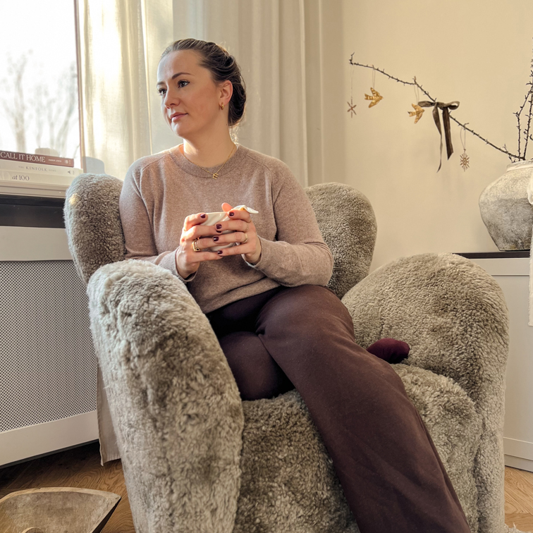 Pohodlné šedé plyšové křeslo s ženou držící šálek v světlém interiéru