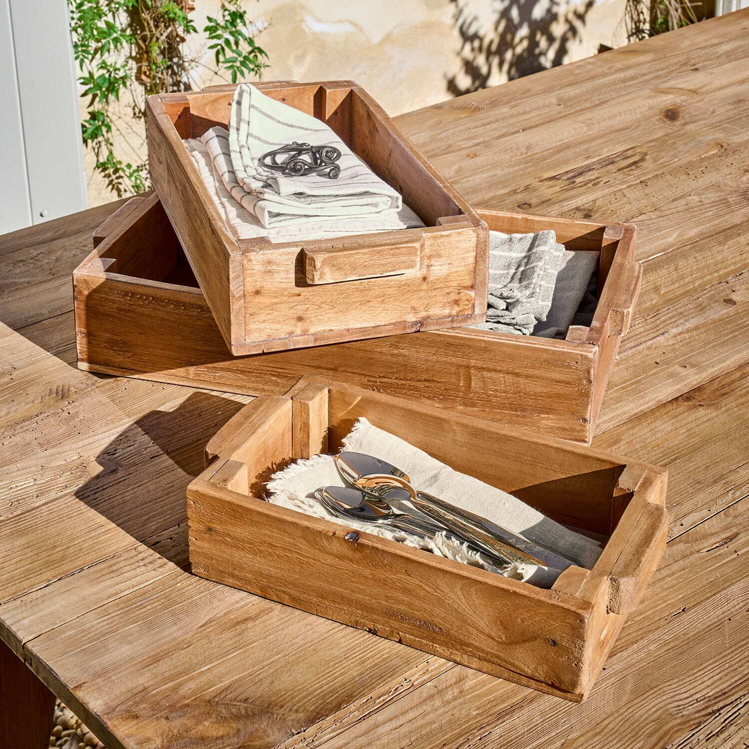 Sada tří dřevěných táců s úchyty v přírodní barvě na dřevěném stole se servítky a příbory