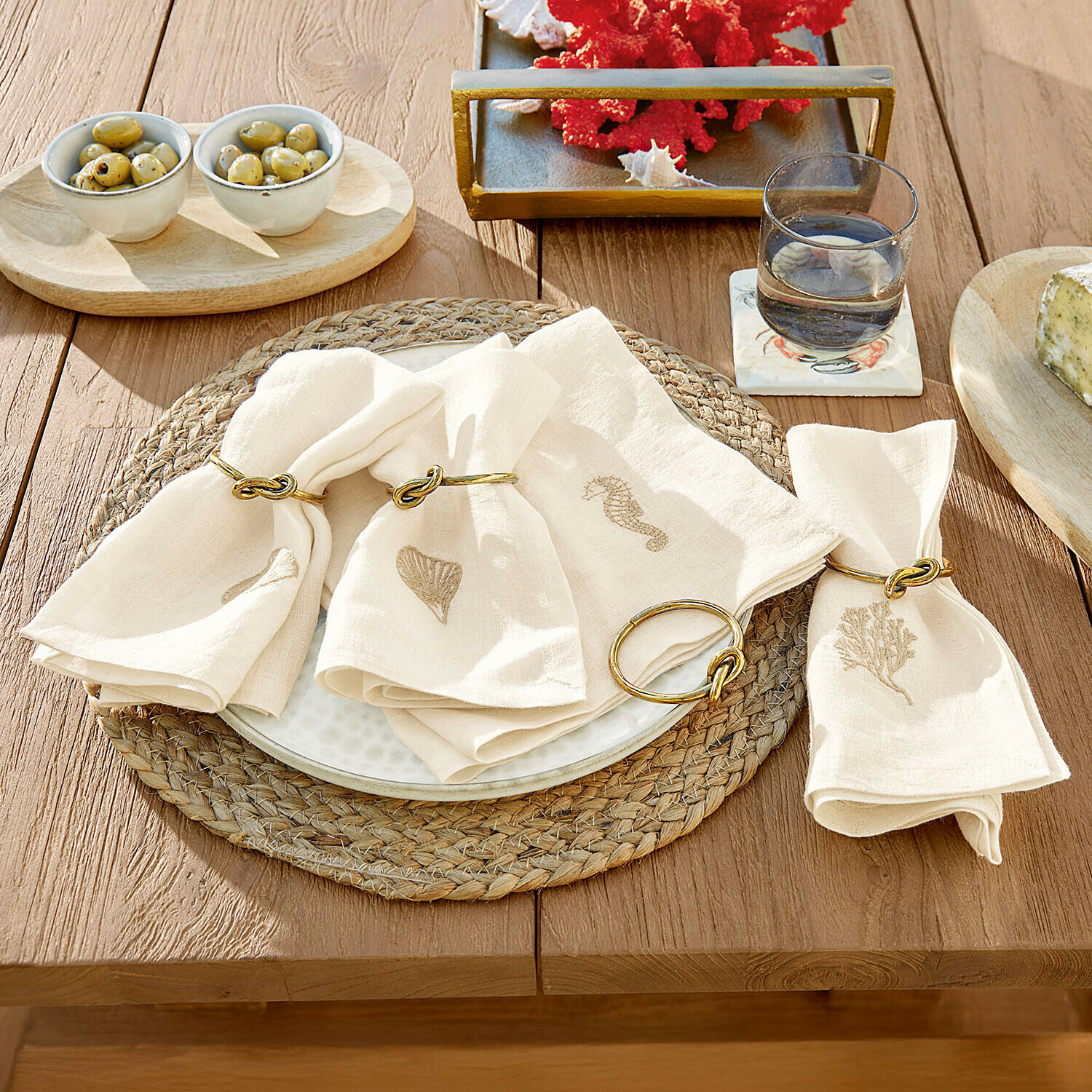 Lněné krémové ubrousky s mořskými motivy a zlatými kroužky na dřevěném stole pro stolní dekoraci
