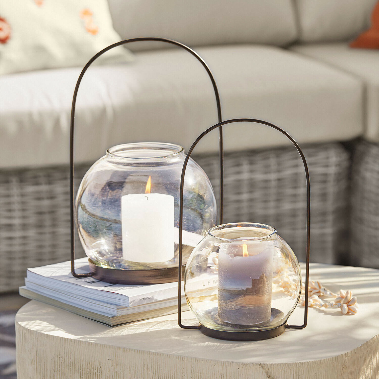 Dvě skleněné lucerny s kovovými držadly a hořícími svíčkami na světlém dekorativním stole