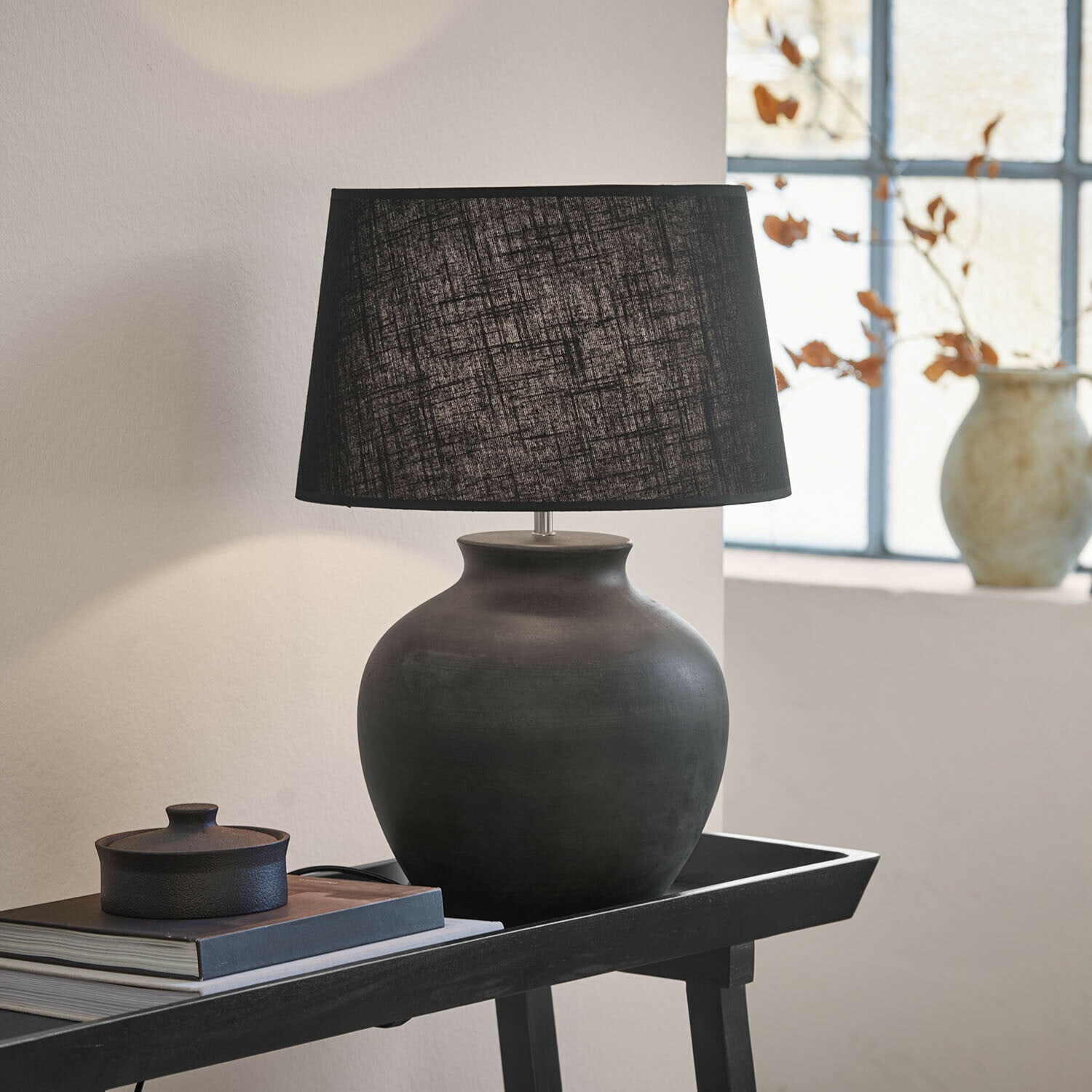 Stolní lampa Branver Černá keramická stolní lampa s textilním stínidlem na stole s knihami a dekorací