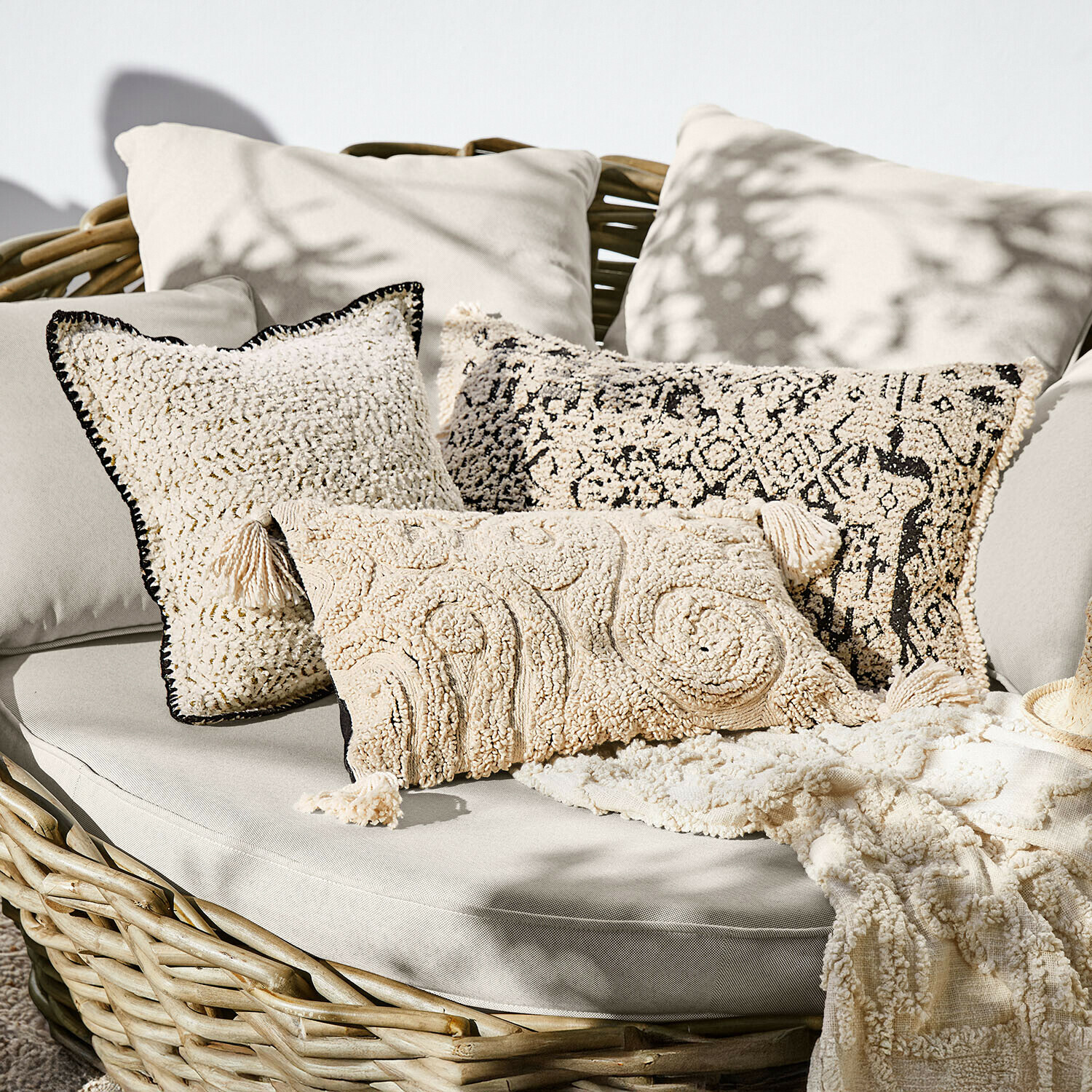 Sada krémových dekorativních polštářů z měkkého materiálu na proutěné pohovce, boho styl