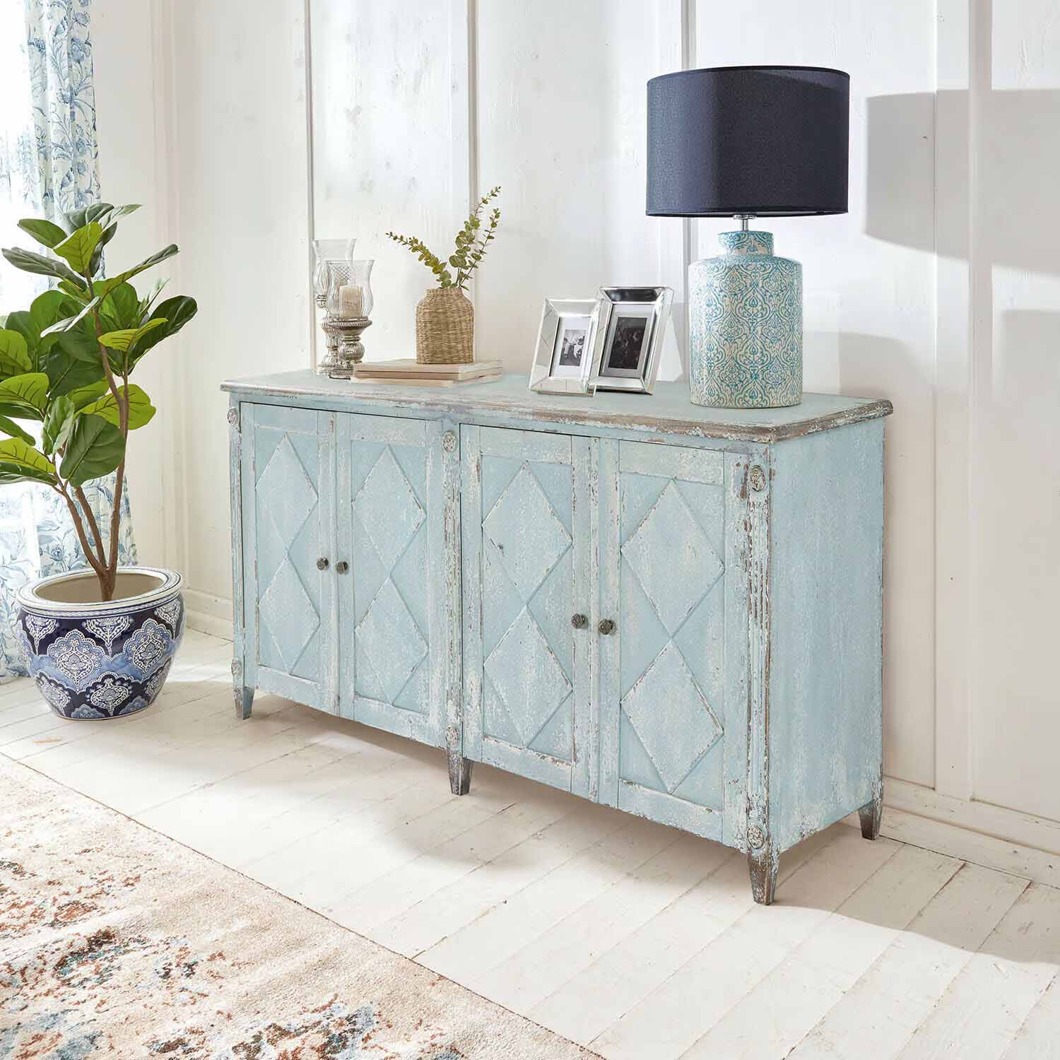 Modrá dřevěná komoda ve vintage stylu s patinou v světlé místnosti s lampou a rostlinou