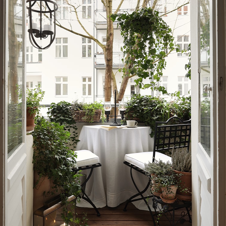 Pohodlný balkon s bílým stolem, černými židlemi a zelenými rostlinami pro relaxaci.