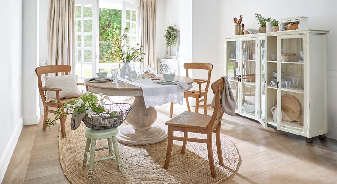 Světý jídelní kout s kulatým dřevěným stolem, rustikálními židlemi a přírodním kobercem pro útulnou atmosféru