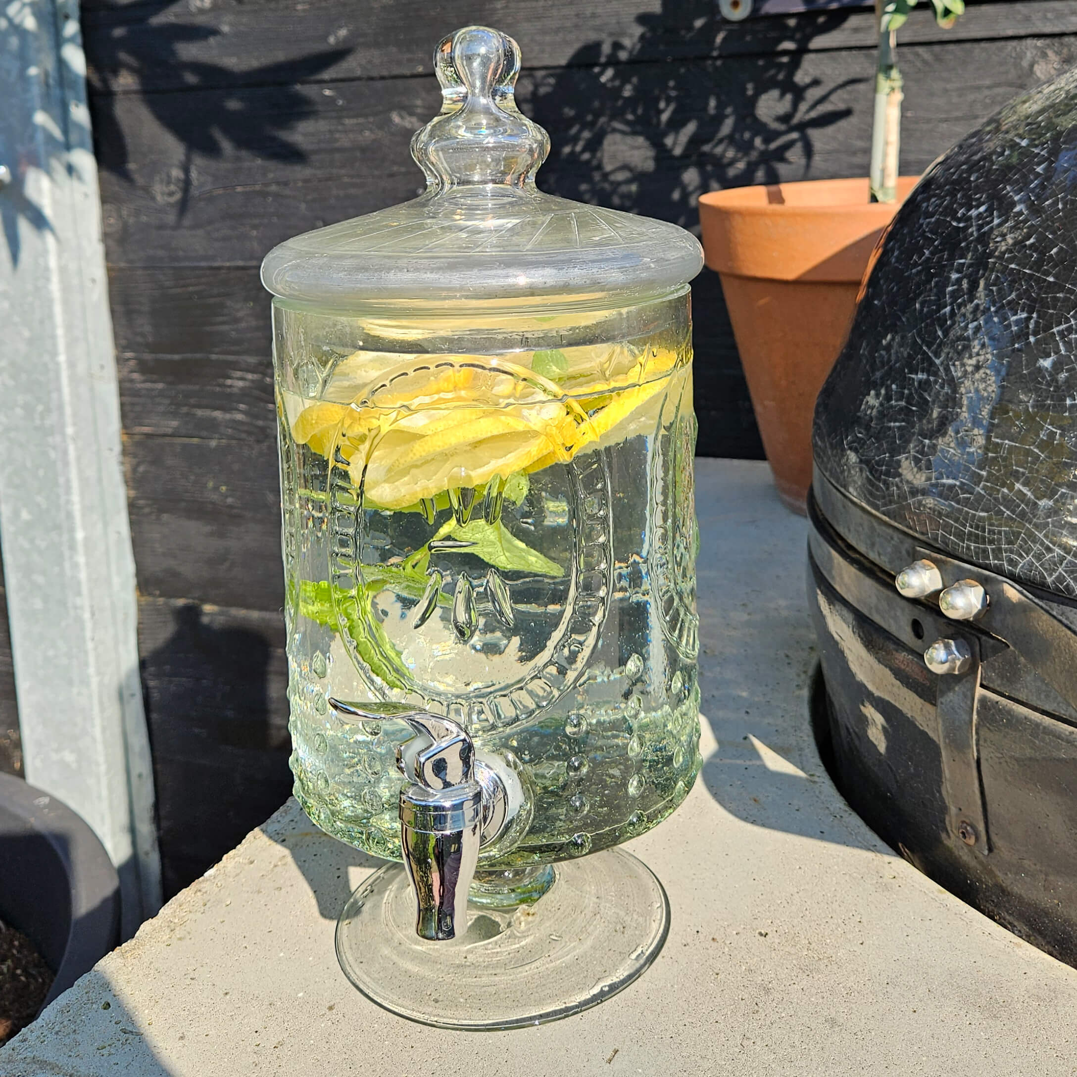 Skleněný nápojový dávkovač s víkem, naplněný vodou s citronem a mátou, vhodný na letní oslavy