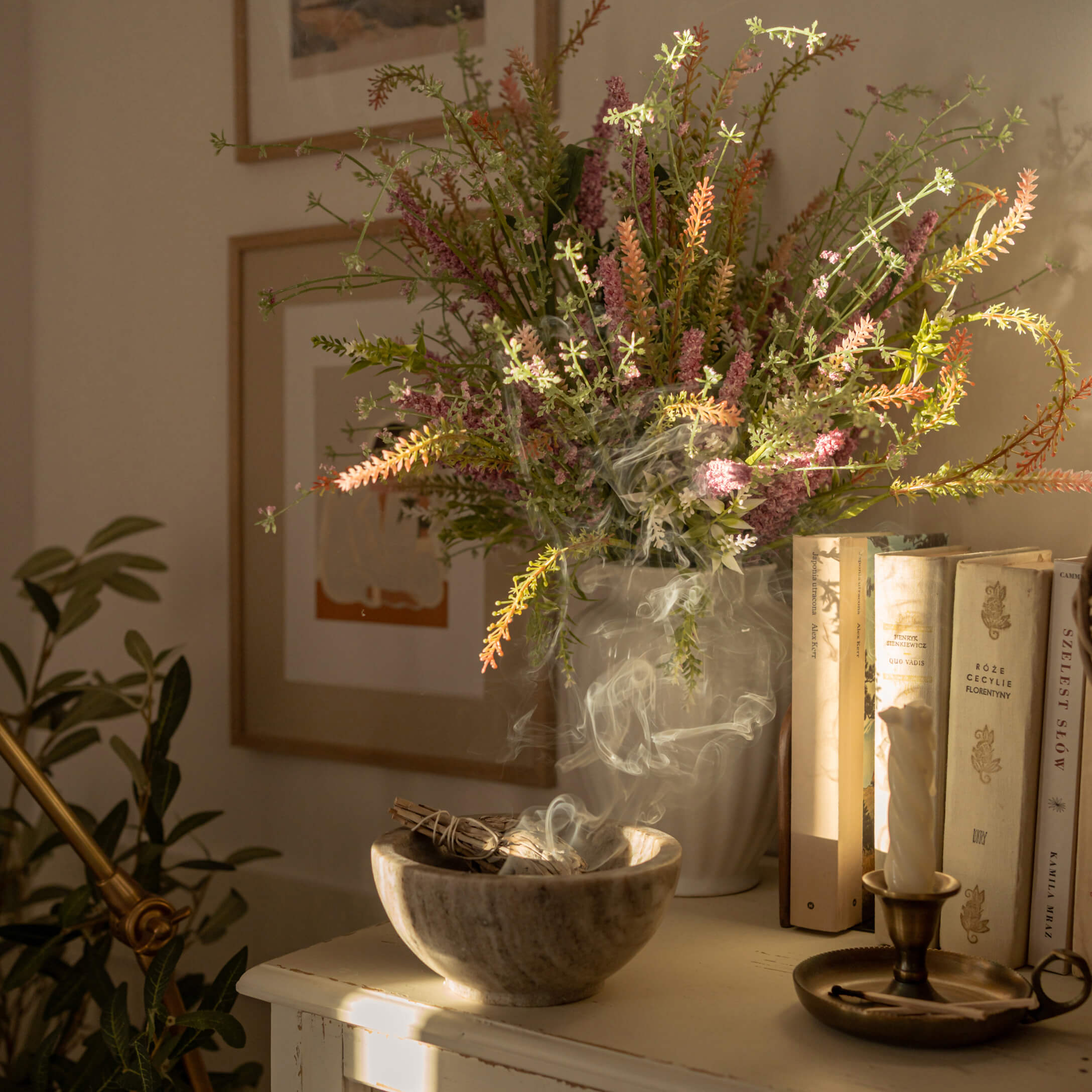 Miska z alabastru s kouřící šalvějí vedle vázy s barevnými květinami a knihami na stole