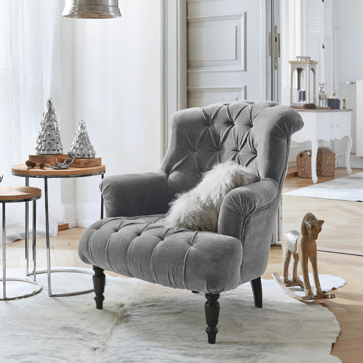 Šedé sametové křeslo s prošívaným opěradlem a černými nohami v světlém obývacím pokoji s vánoční výzdobou