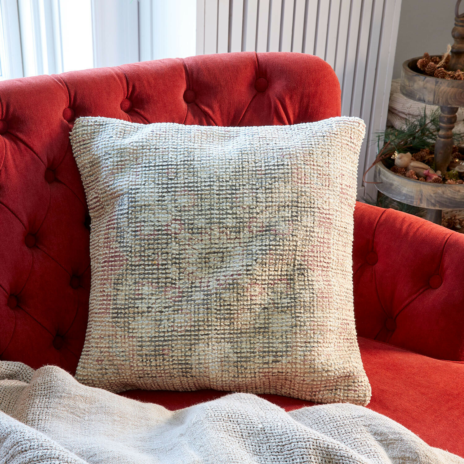 Béžový dekorativní polštář z měkkého materiálu na červené prošívané pohovce v obývacím pokoji